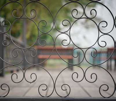 Un primer plano de una valla de hierro forjado con un banco al fondo.
