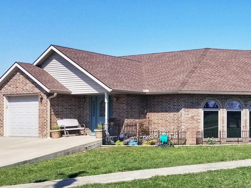 Single-story brick house with a brown shingled roof, attached garage, and blue front door under a clear blue sky.
