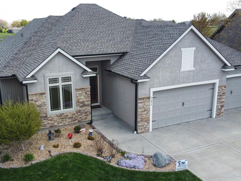 A single-story suburban house with a gray exterior, stone accents, a multi-car garage, and a landscaped front yard.