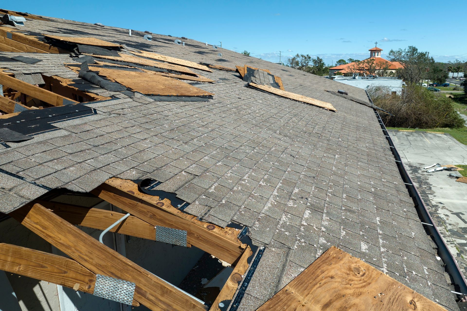 A damaged roof with missing shingles and exposed wooden trusses on a sunny day.