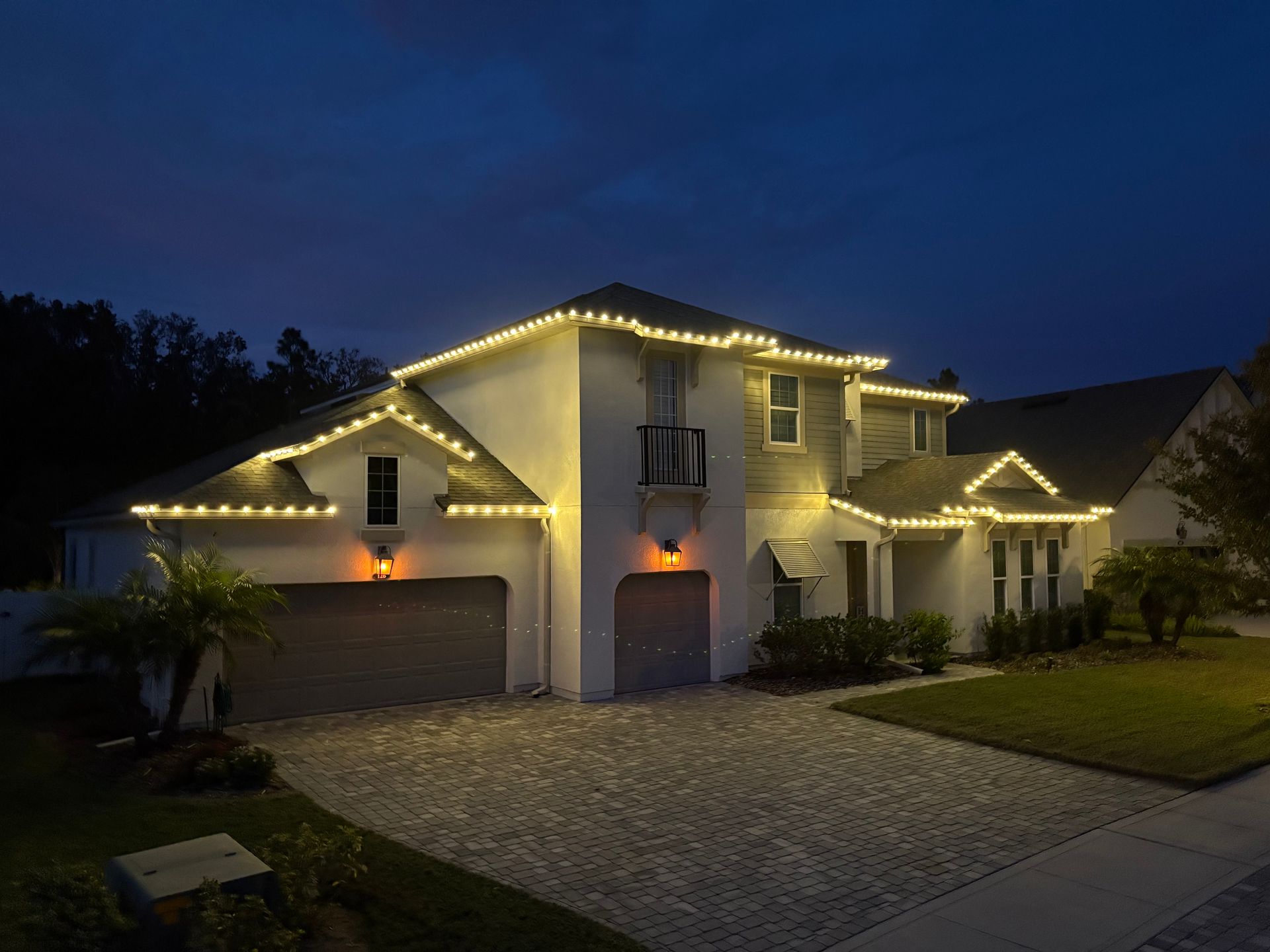 House with warm white Christmas lights outlining roof and windows at dusk.