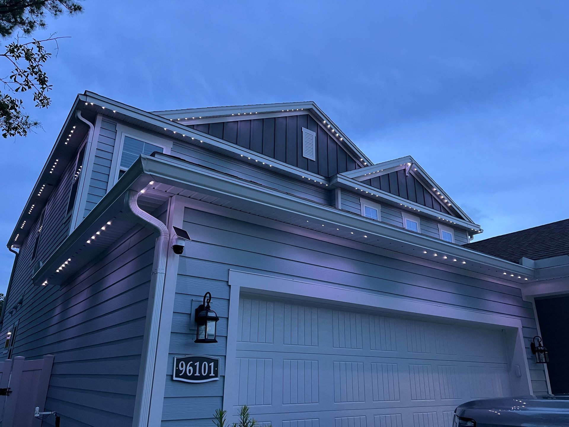 Blue house with white garage door and roofline lights under a cloudy sky.