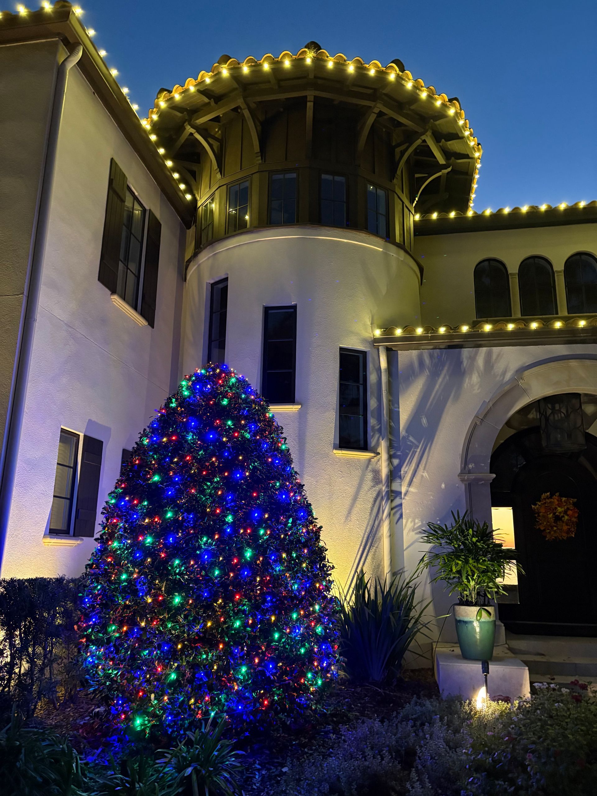 A house decorated with string lights, and a Christmas tree with colorful lights.