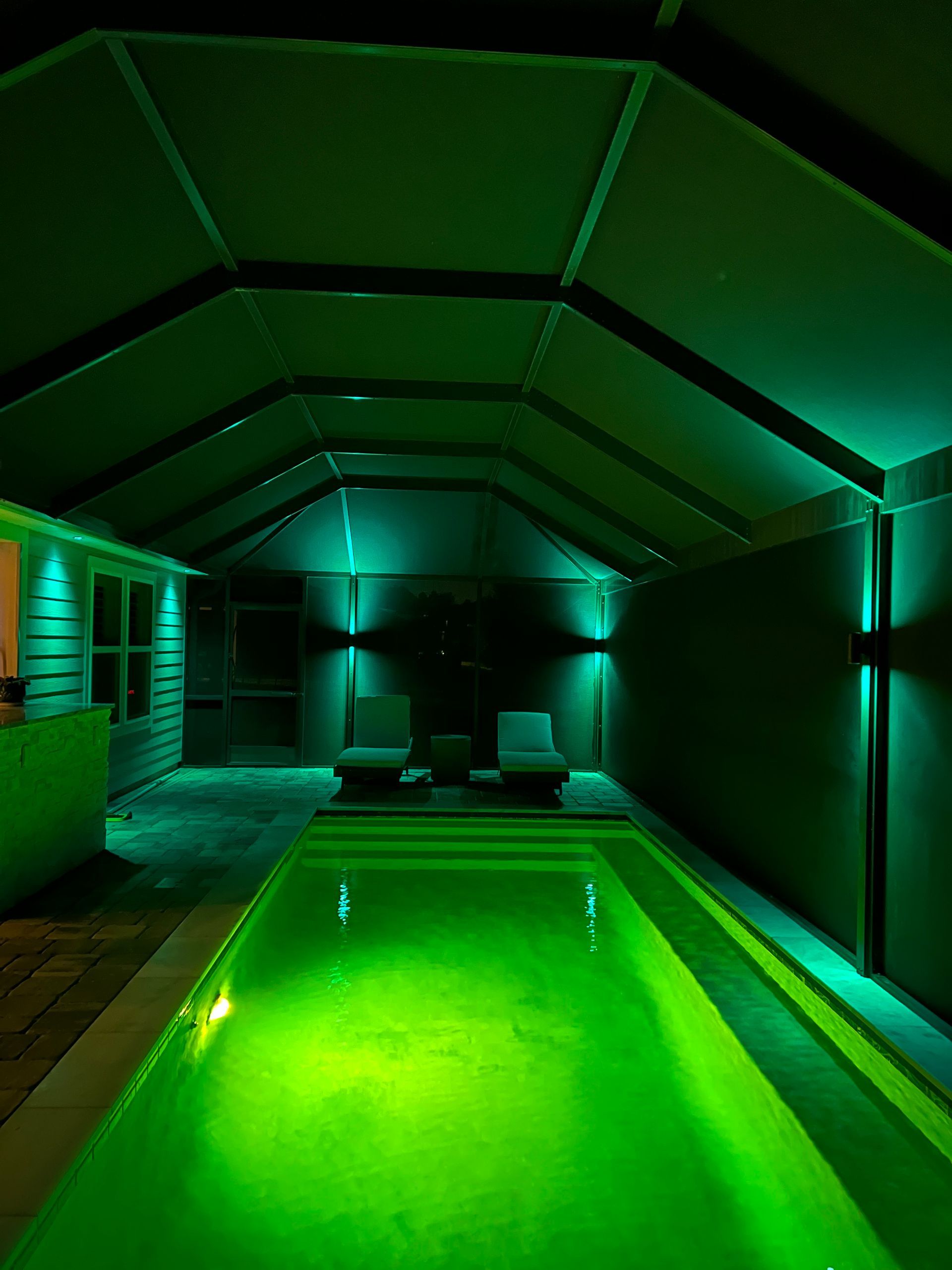 Green-lit indoor pool with two chairs. Dark room with angled ceiling.