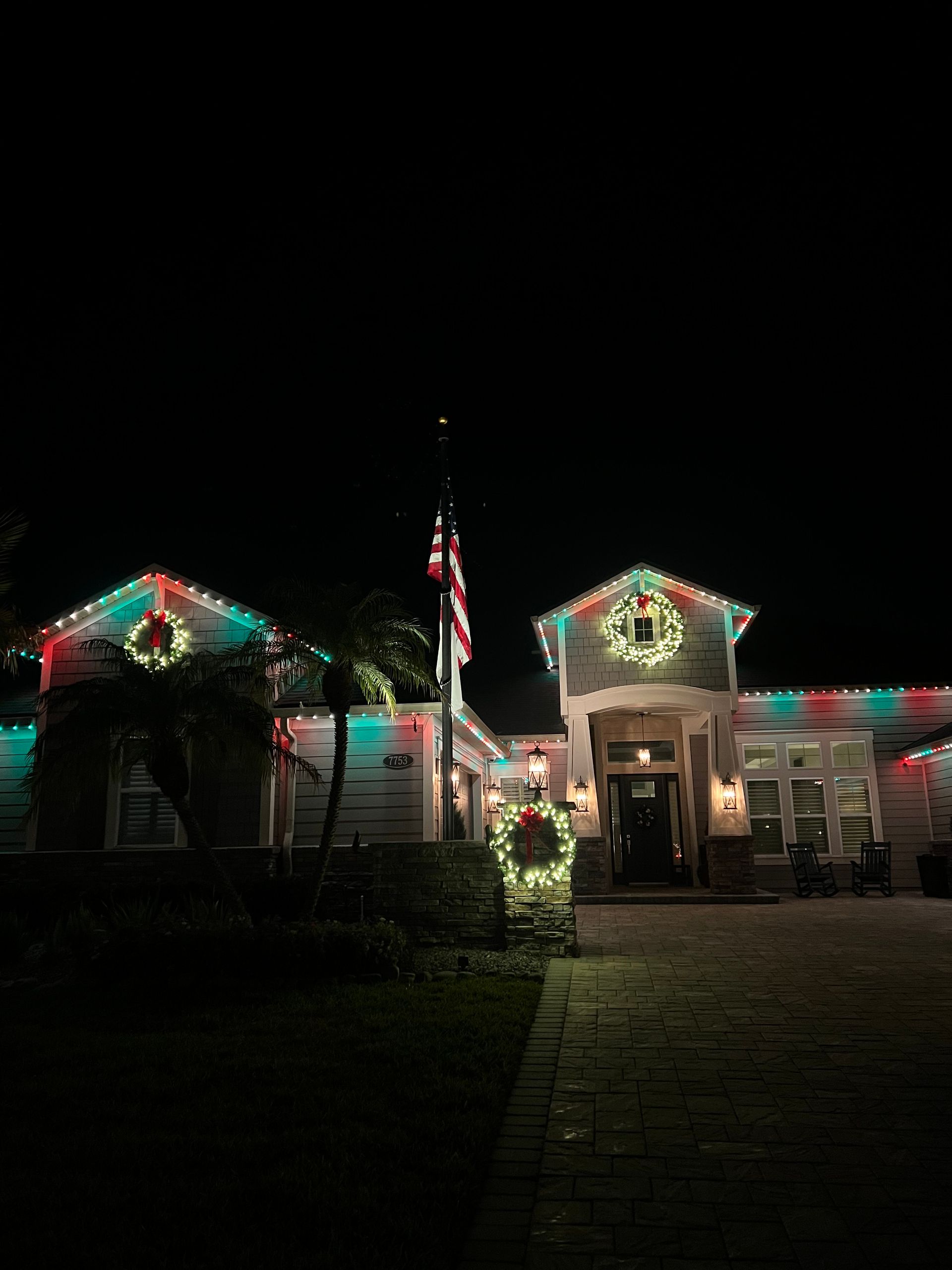 House decorated for the holidays with red and green lights and wreaths. Flagpole in the middle.