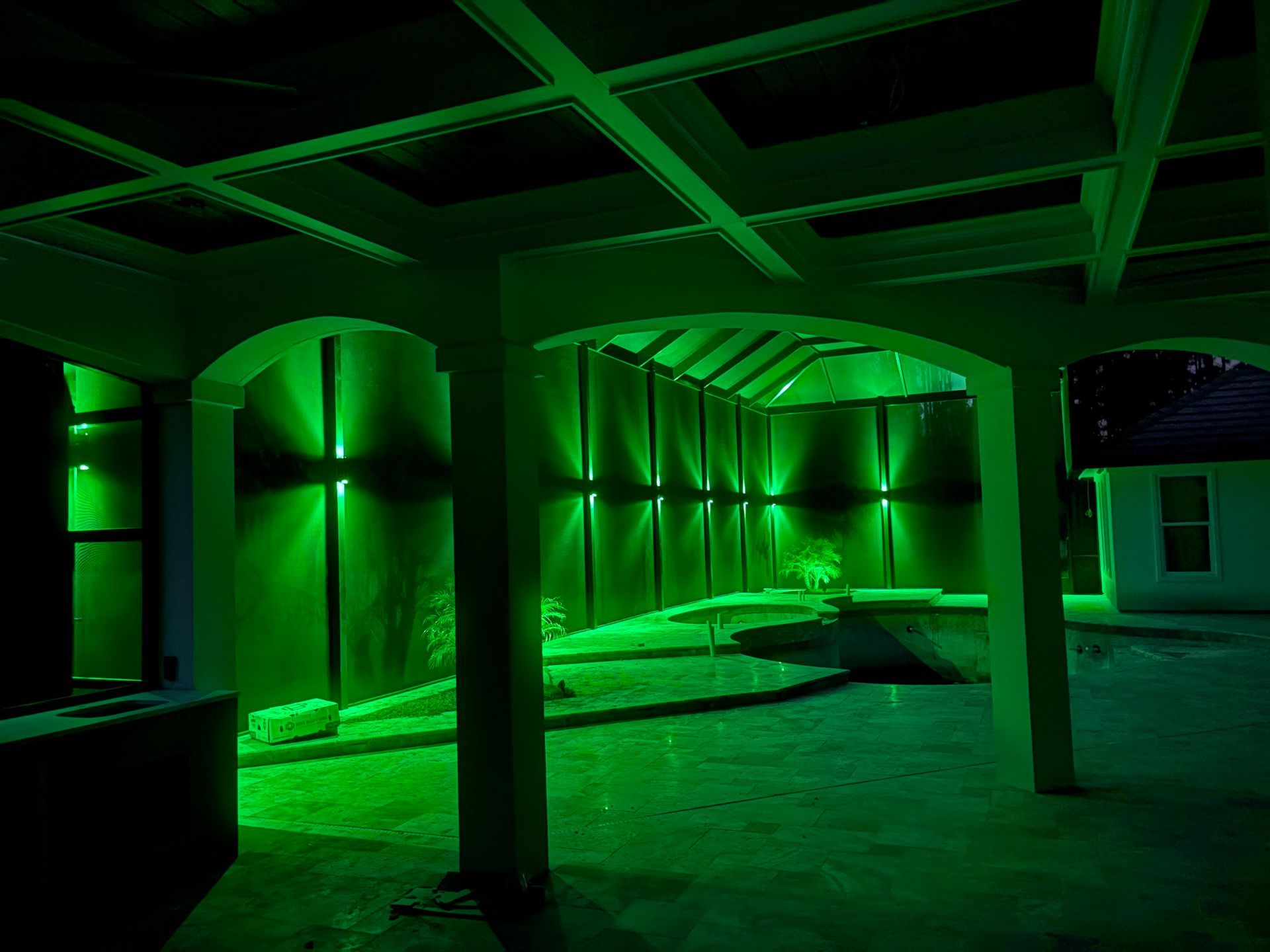 Green outdoor lighting illuminating a patio and backyard with pillars and a fence.