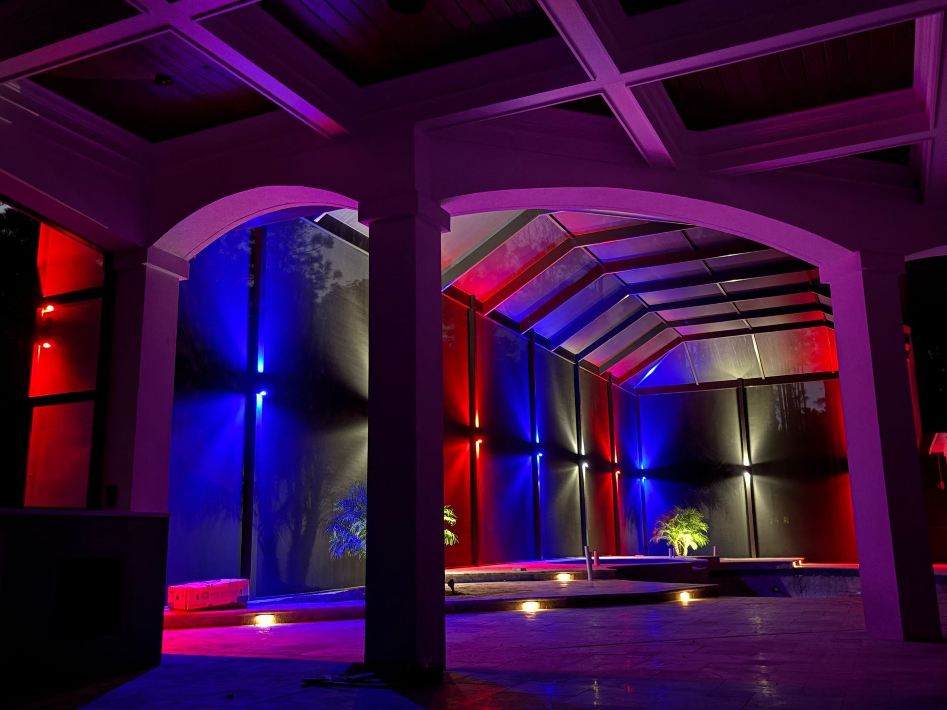 Red and blue lit interior of a building with arches and columns, a water feature, and a sloped ceiling.
