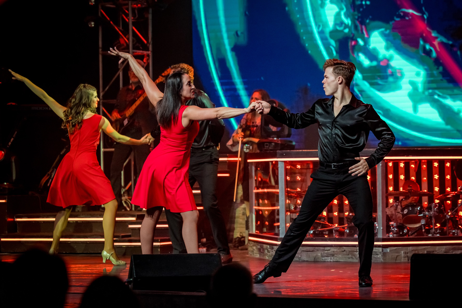 A group of people are dancing on a stage in front of a large screen.