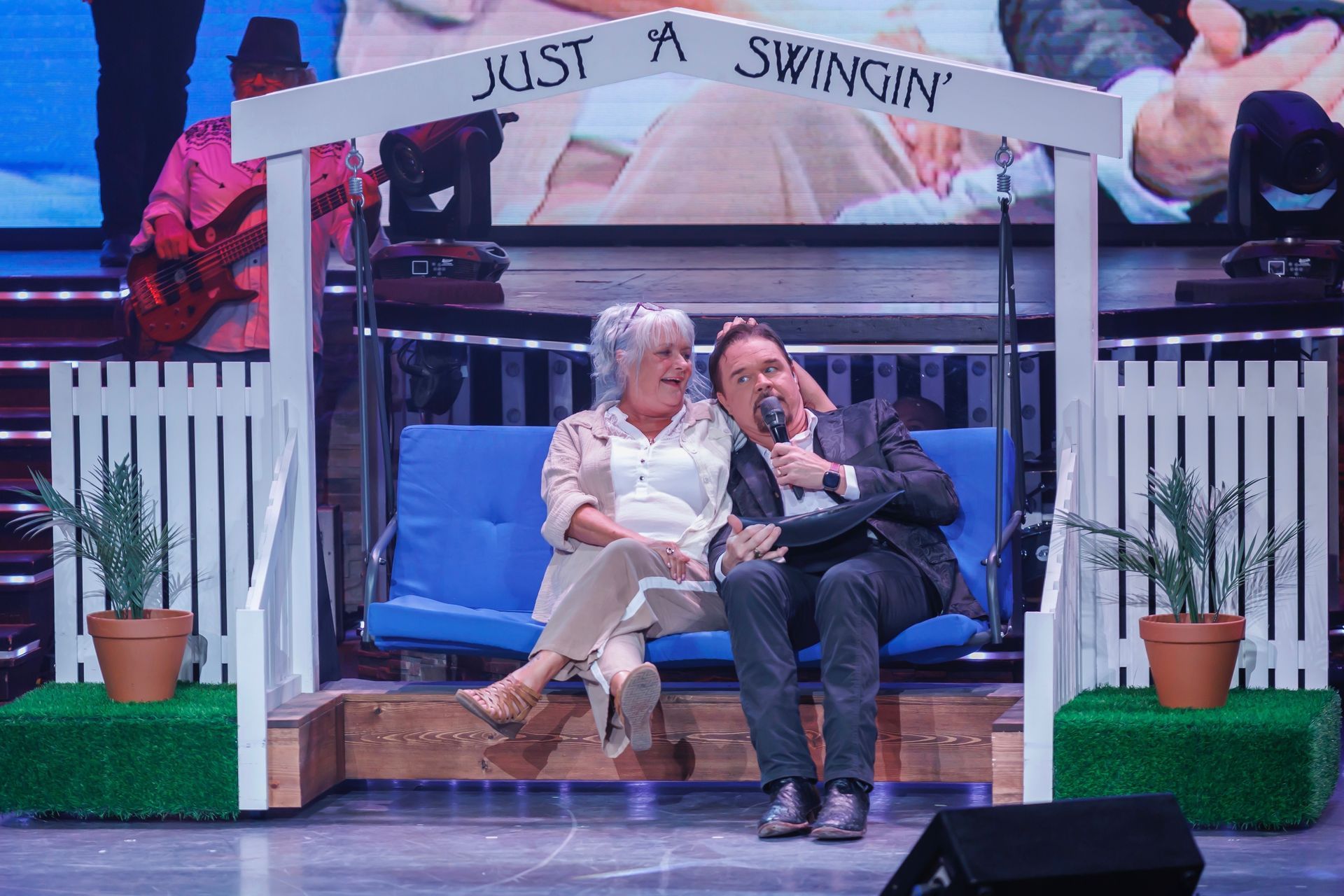 A man and a woman are sitting on a blue bench under a sign that says just a swingin '