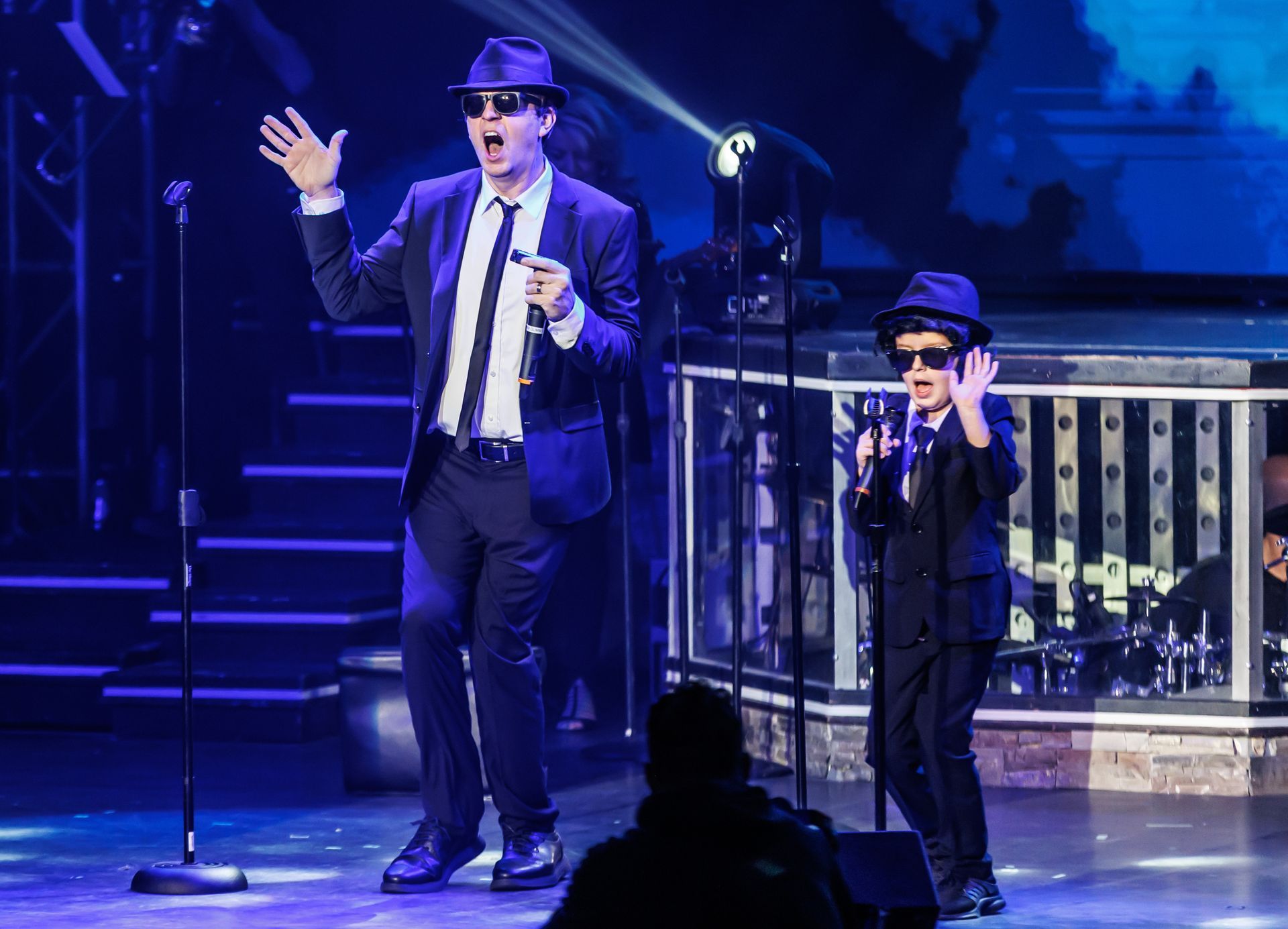 Two people in Blues Brothers costumes perform on stage.