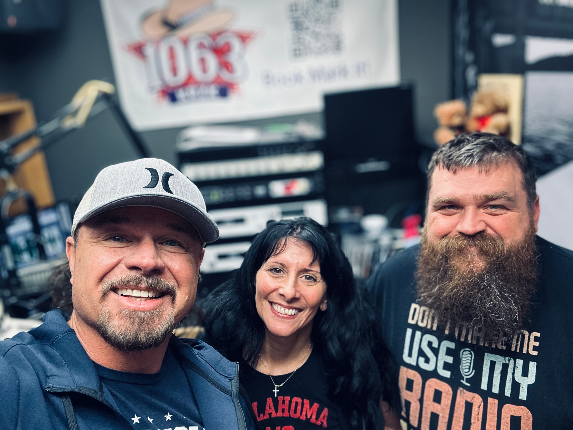 Three people smiling in a radio studio. A 