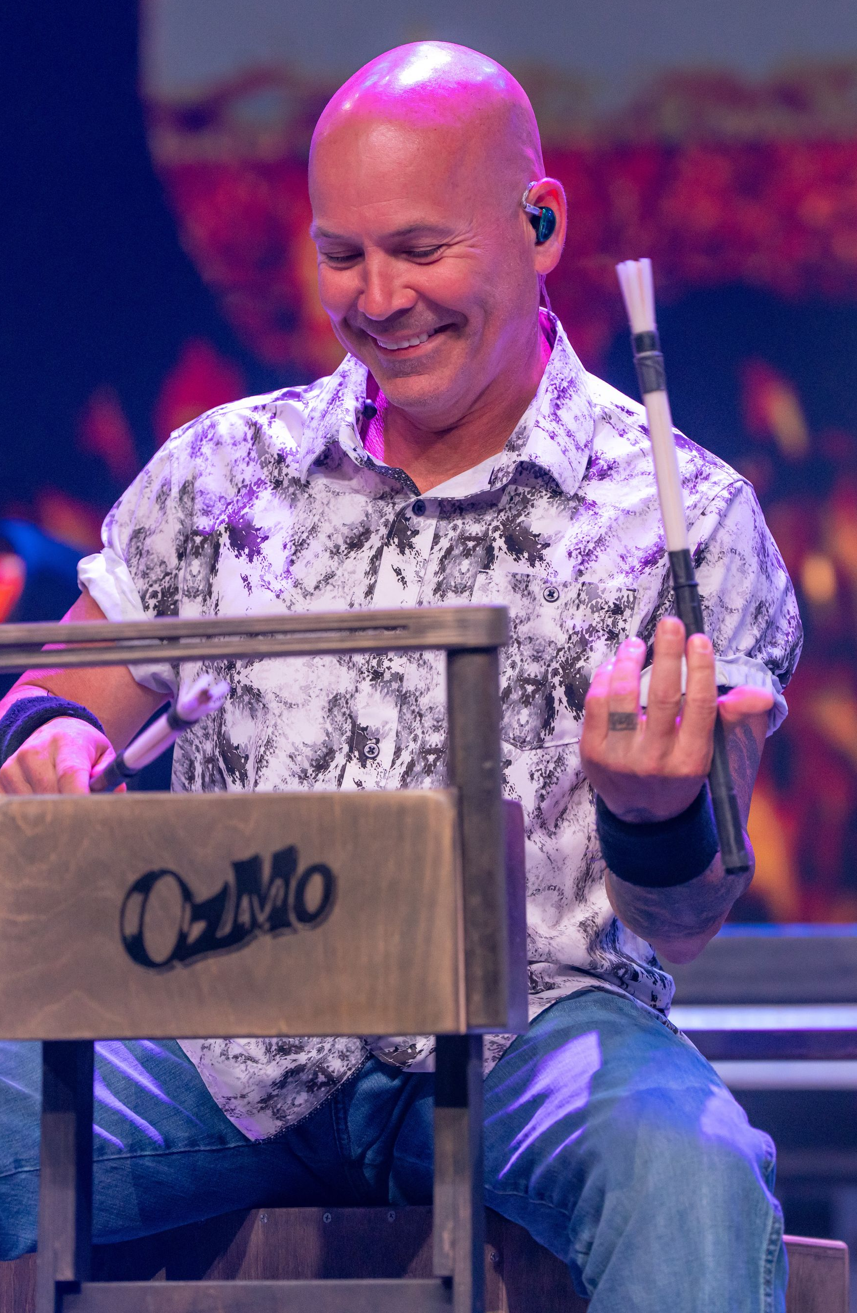 Man wearing a cap, performing music on a cajon. He is in a dim setting, with a microphone nearby.