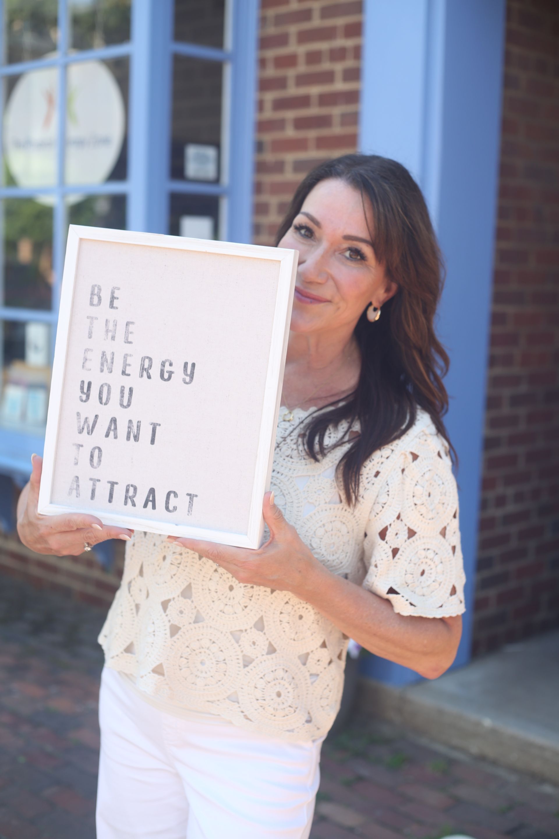 A woman is holding a sign that says `` be the energy you want to attract ''.