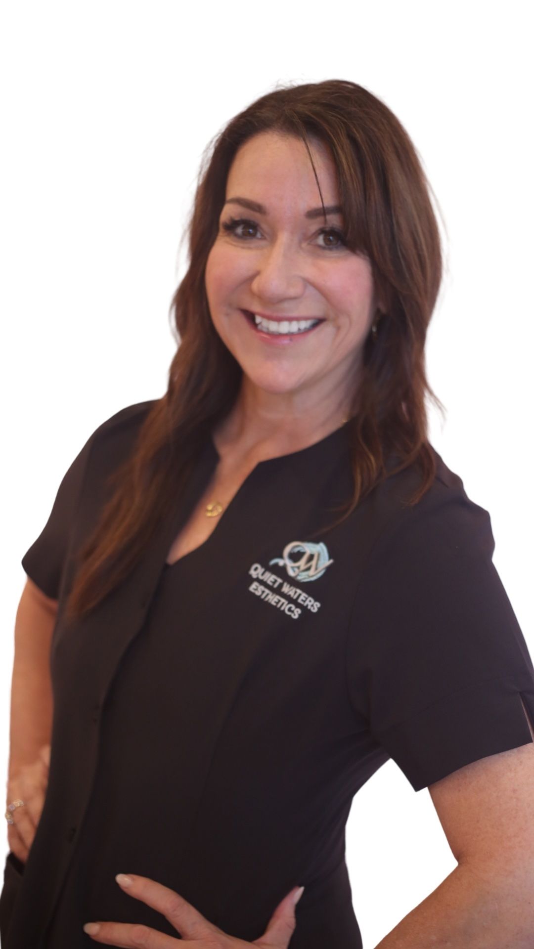 A woman in a black scrub top is smiling and standing with her hands on her hips.