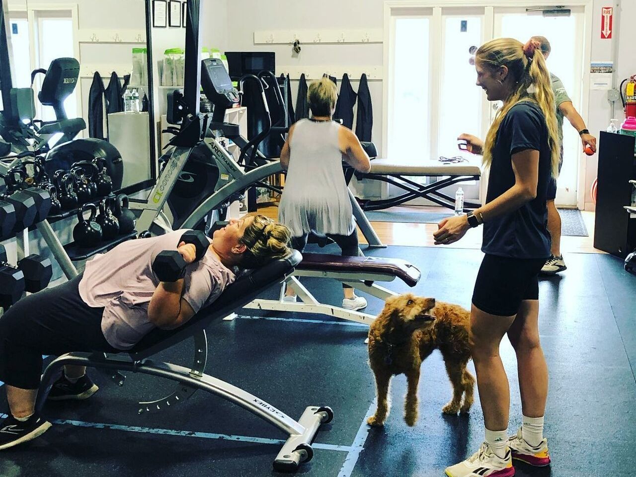 A man is stretching a woman 's leg in a gym.