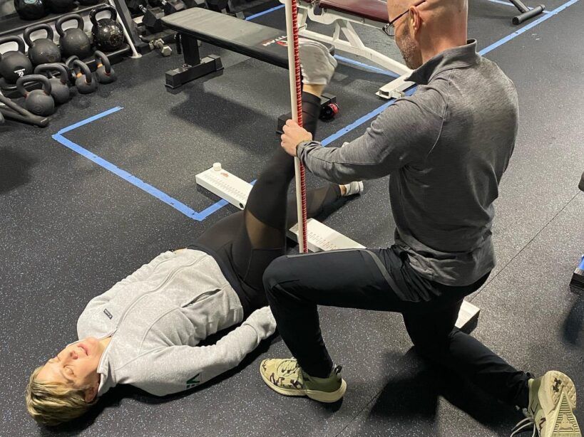 A man is stretching a woman 's leg in a gym.