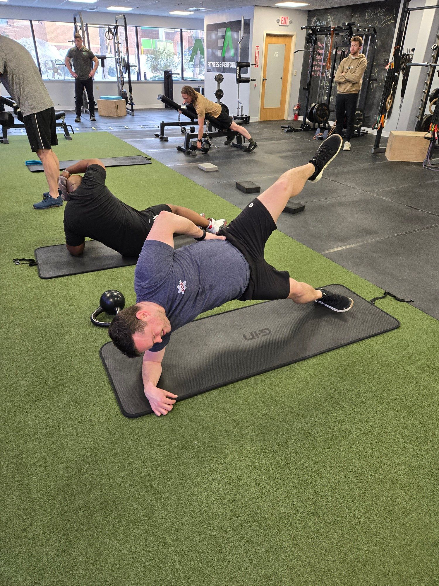 A man is stretching a woman 's leg in a gym.
