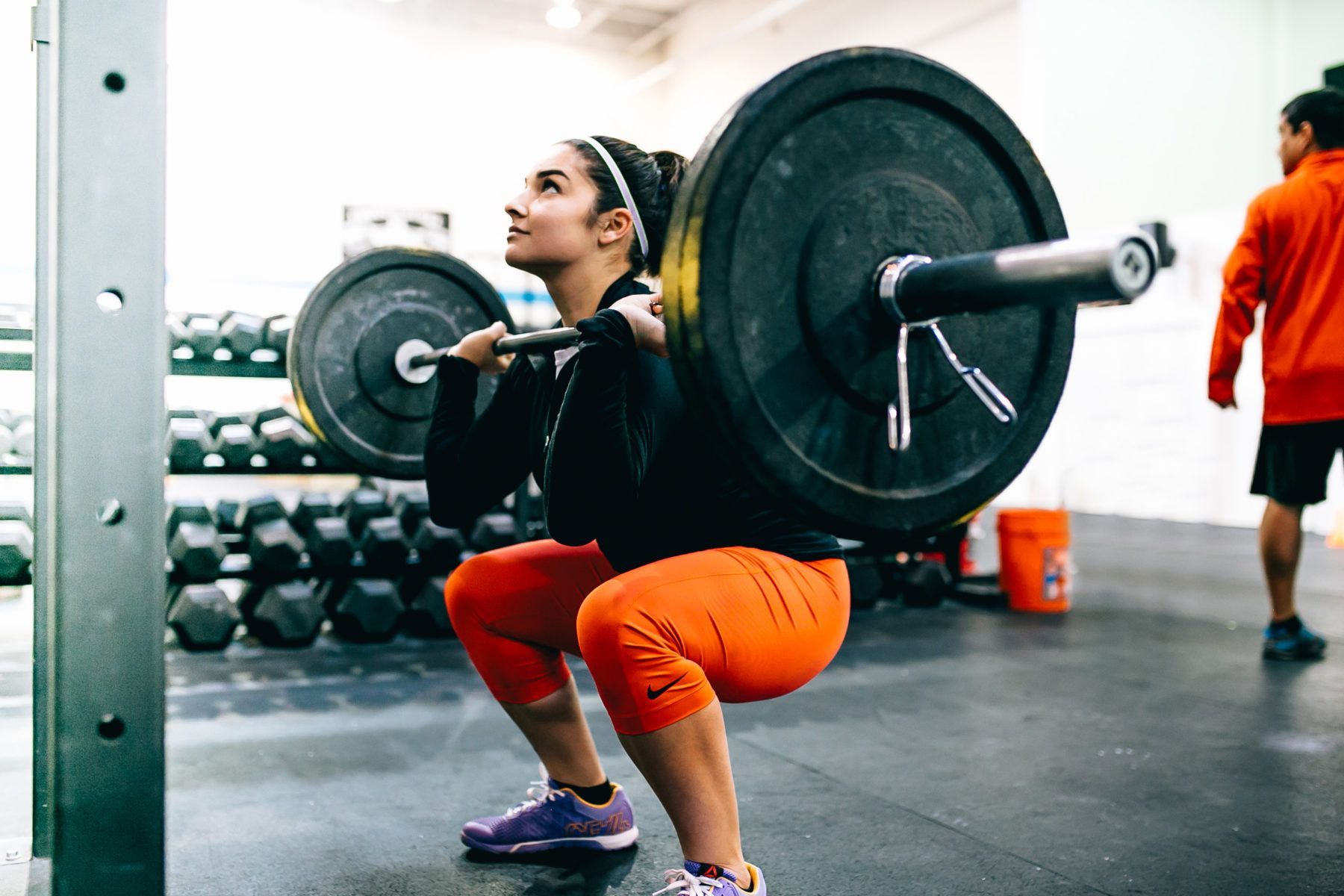 A woman is squatting with a barbell over her head in a gym.