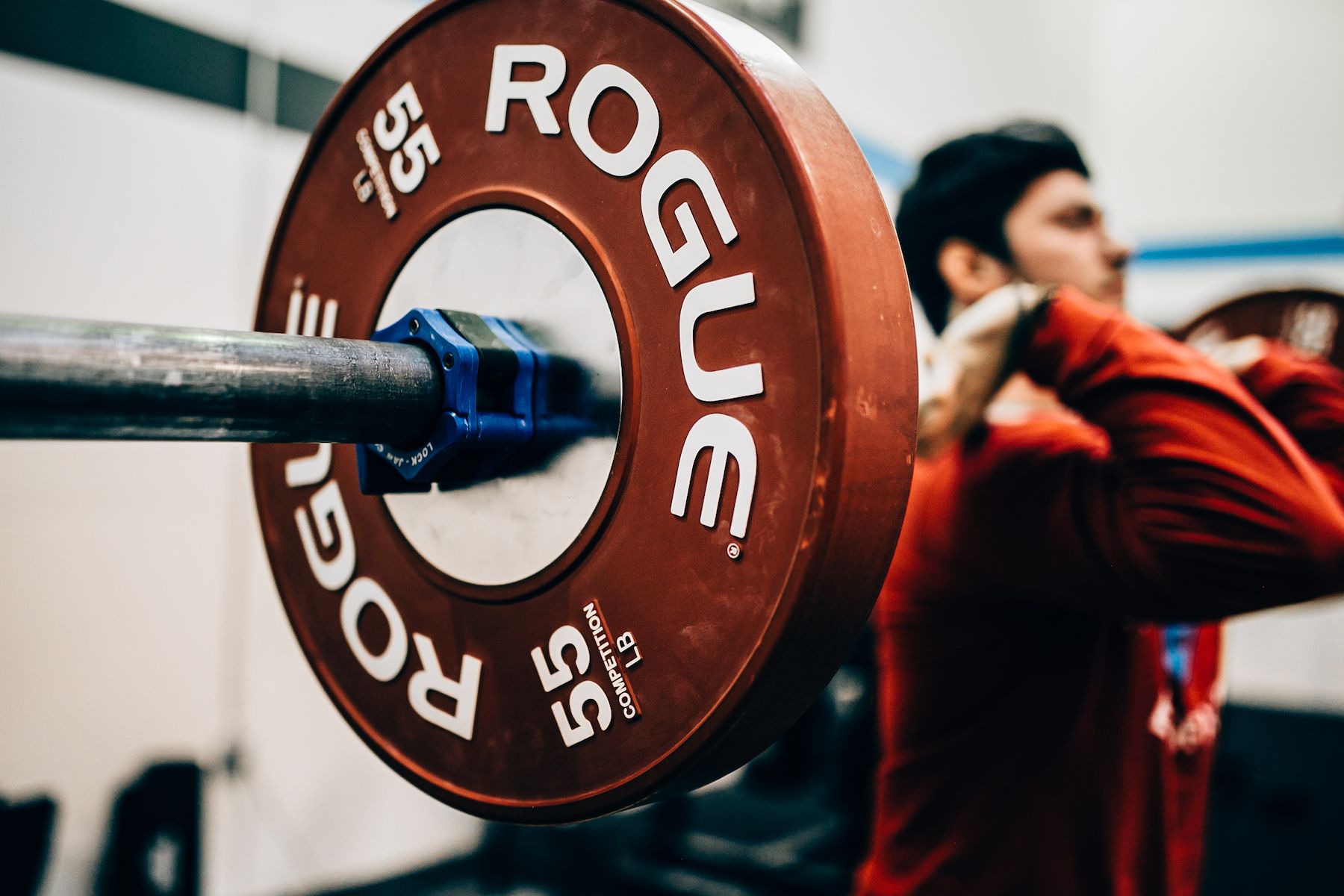 A man is squatting with a barbell that says rogue on it.