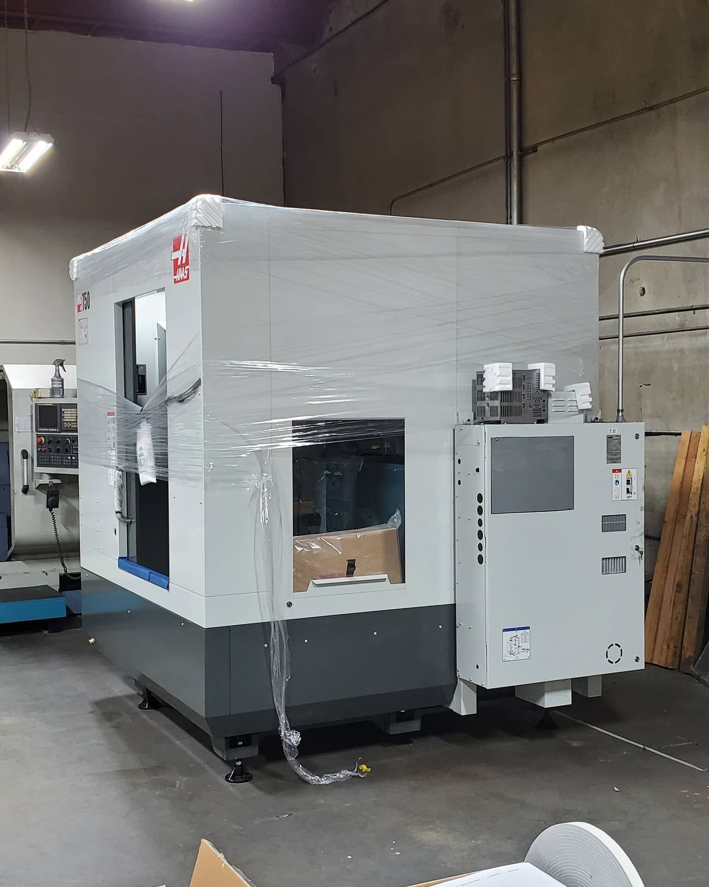 CNC machining center in a workshop, wrapped in plastic. Gray and white colors.