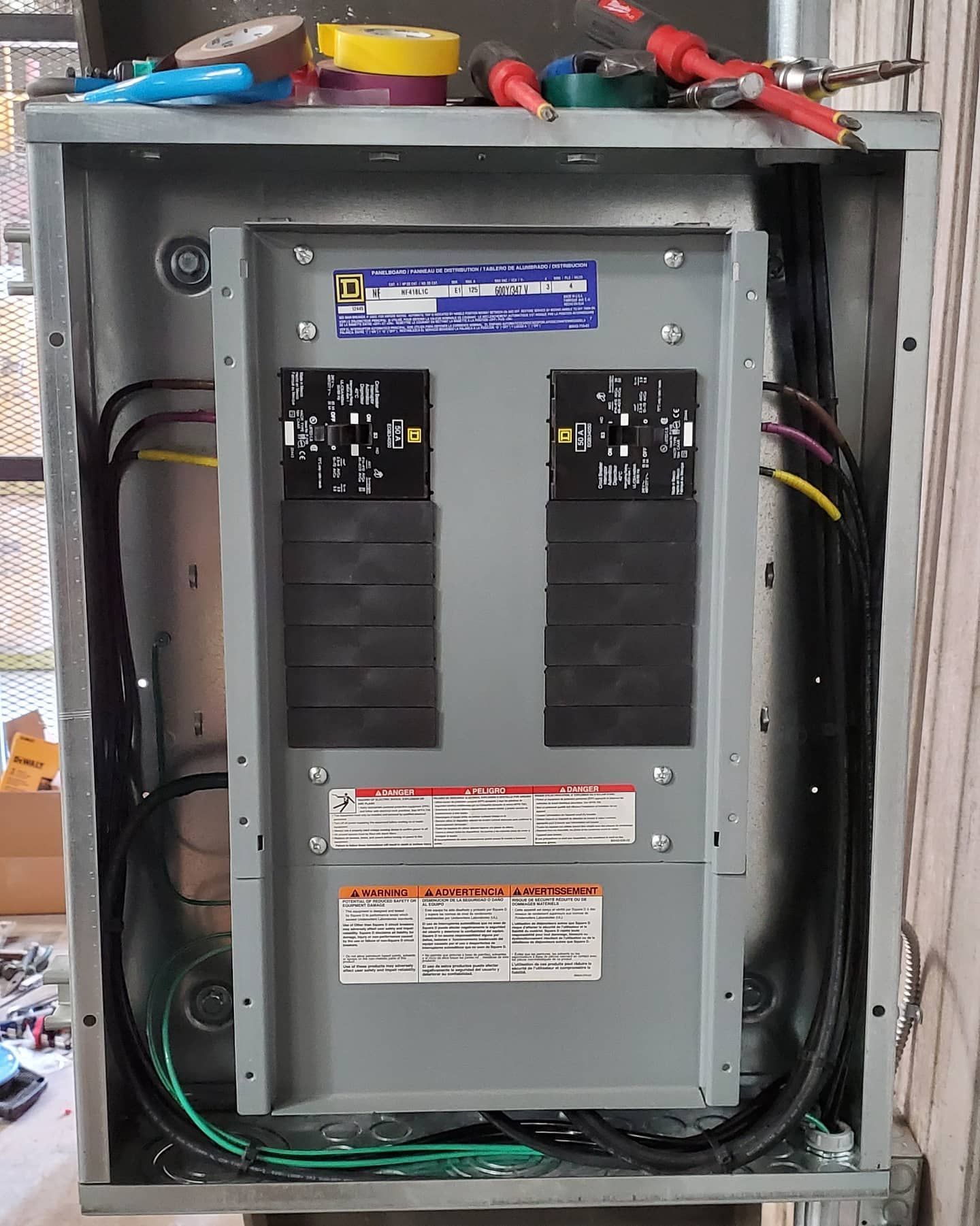 Electrical panel with circuit breakers, wires, and tools on top.