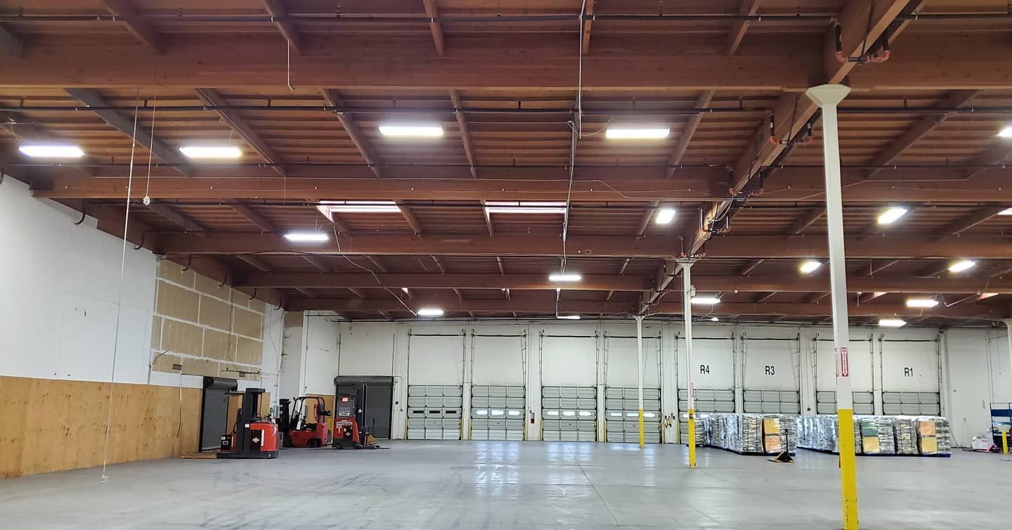 Interior of a warehouse with a high wooden ceiling, loading dock doors, and pallets.