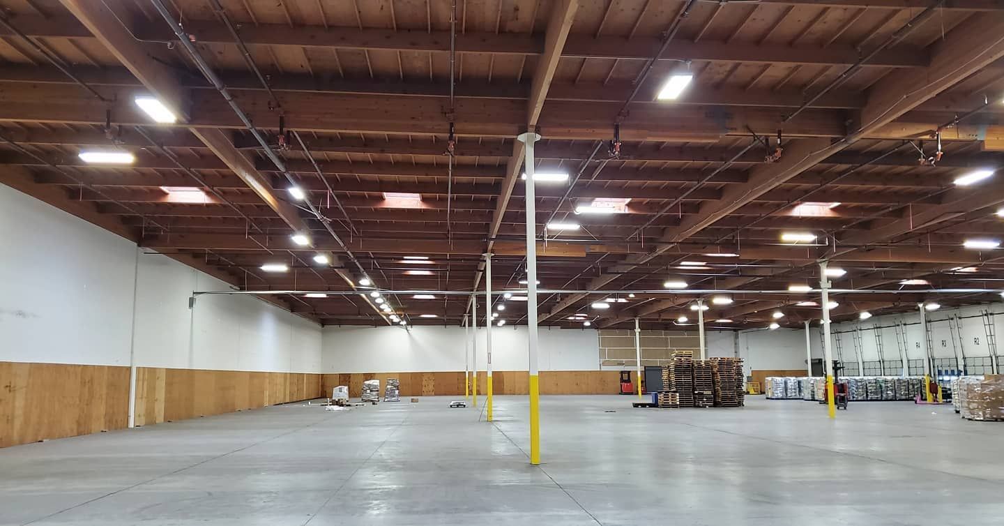 Empty warehouse interior with wood beams, concrete floor, and fluorescent lights.