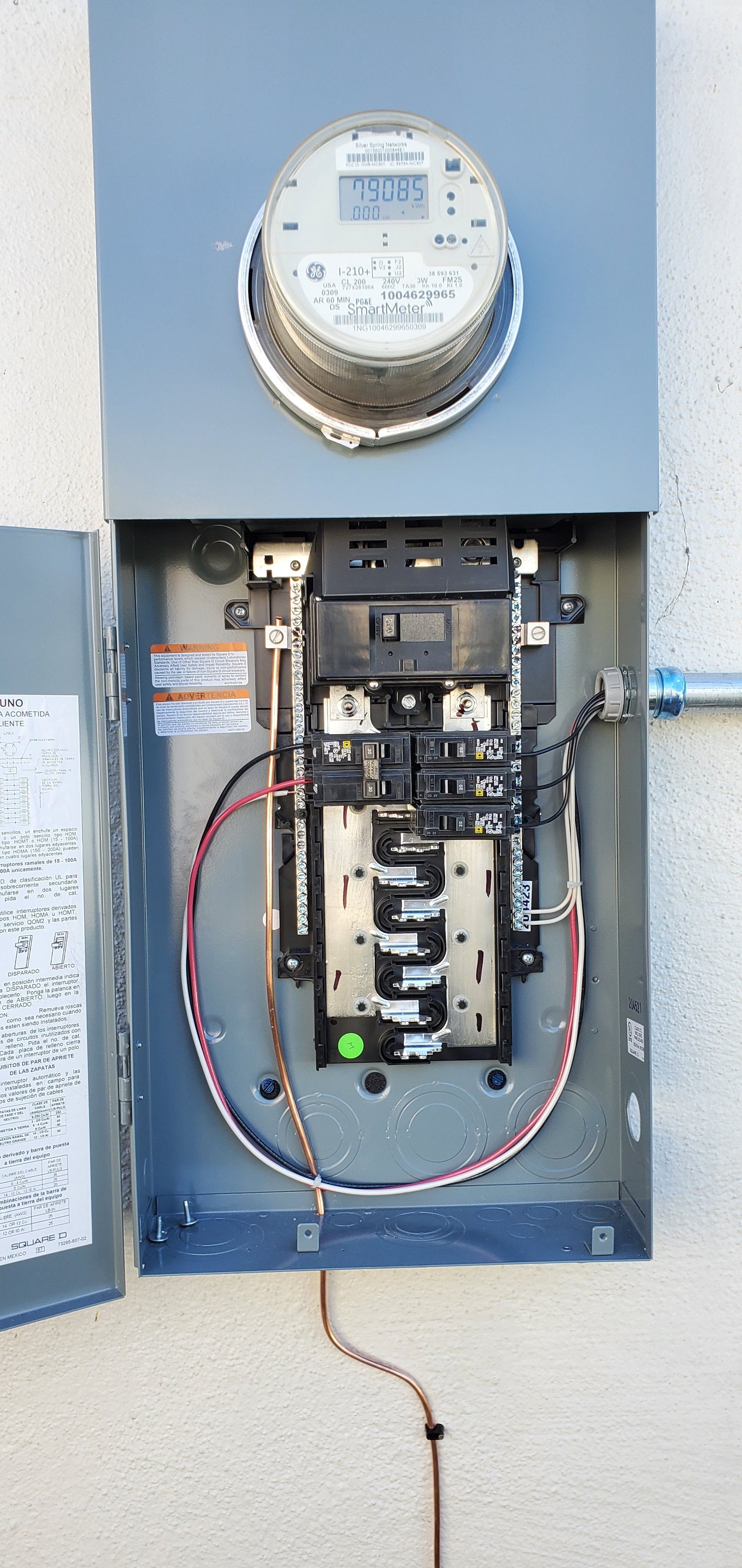 Electrical panel mounted on a light-colored wall, with the panel door open revealing circuit breakers and wiring.