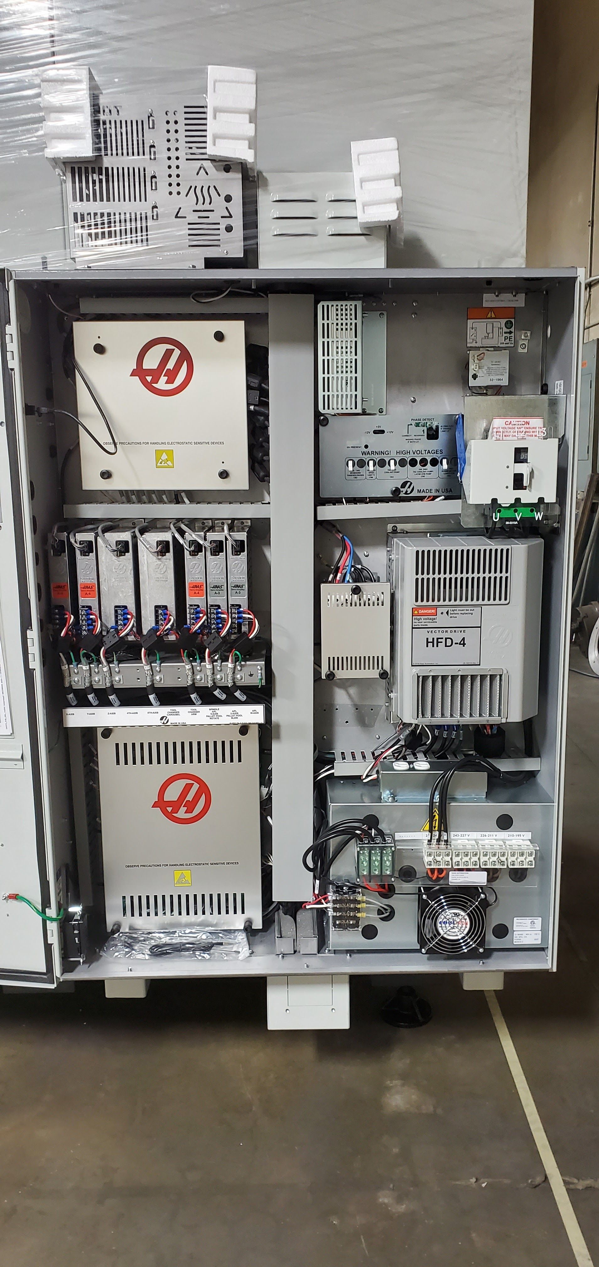 An open electrical cabinet with various components, including Haas and ABB equipment, wiring, and a cooling fan.
