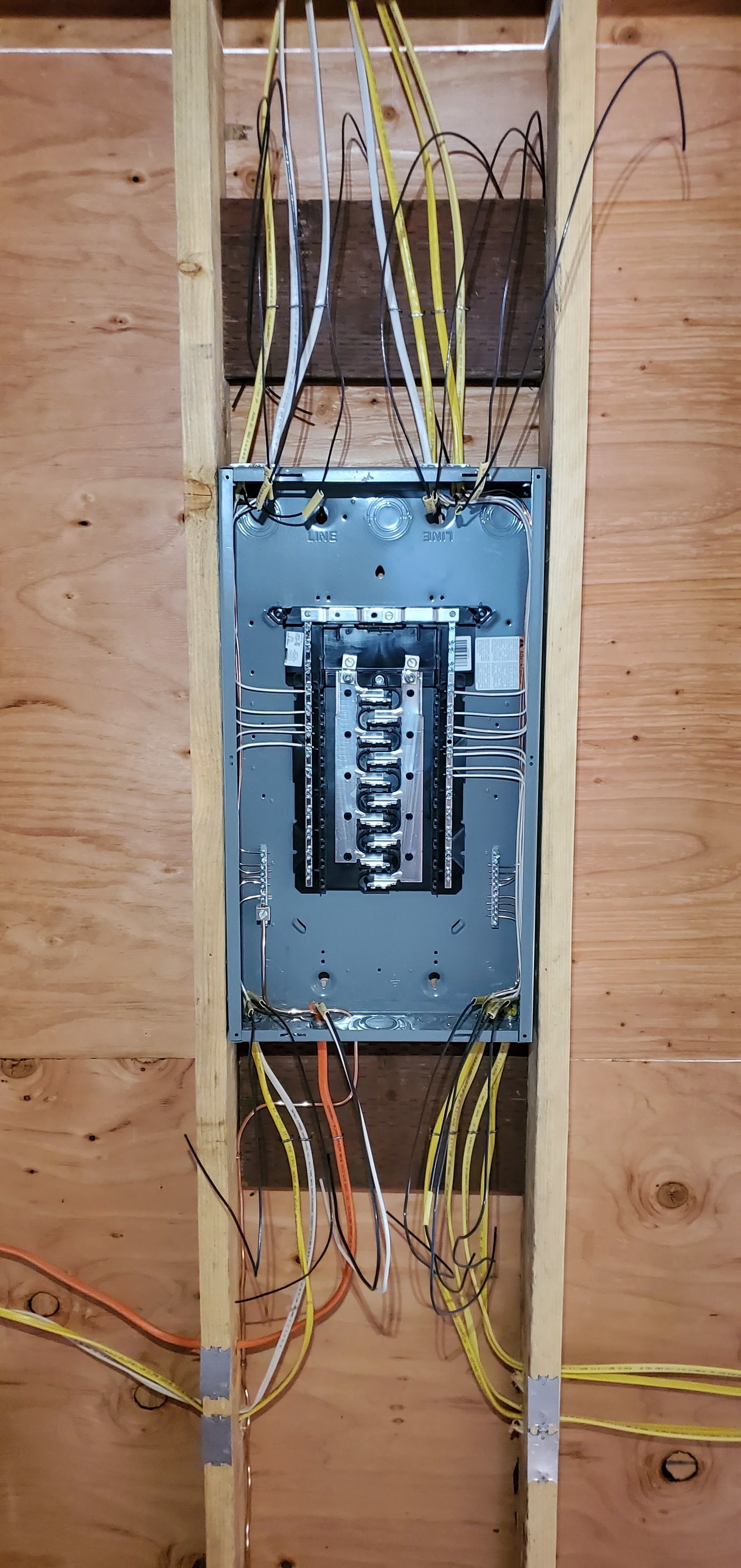 Electrical panel with exposed wires, mounted in a wooden frame. Wires are yellow, white, and orange.