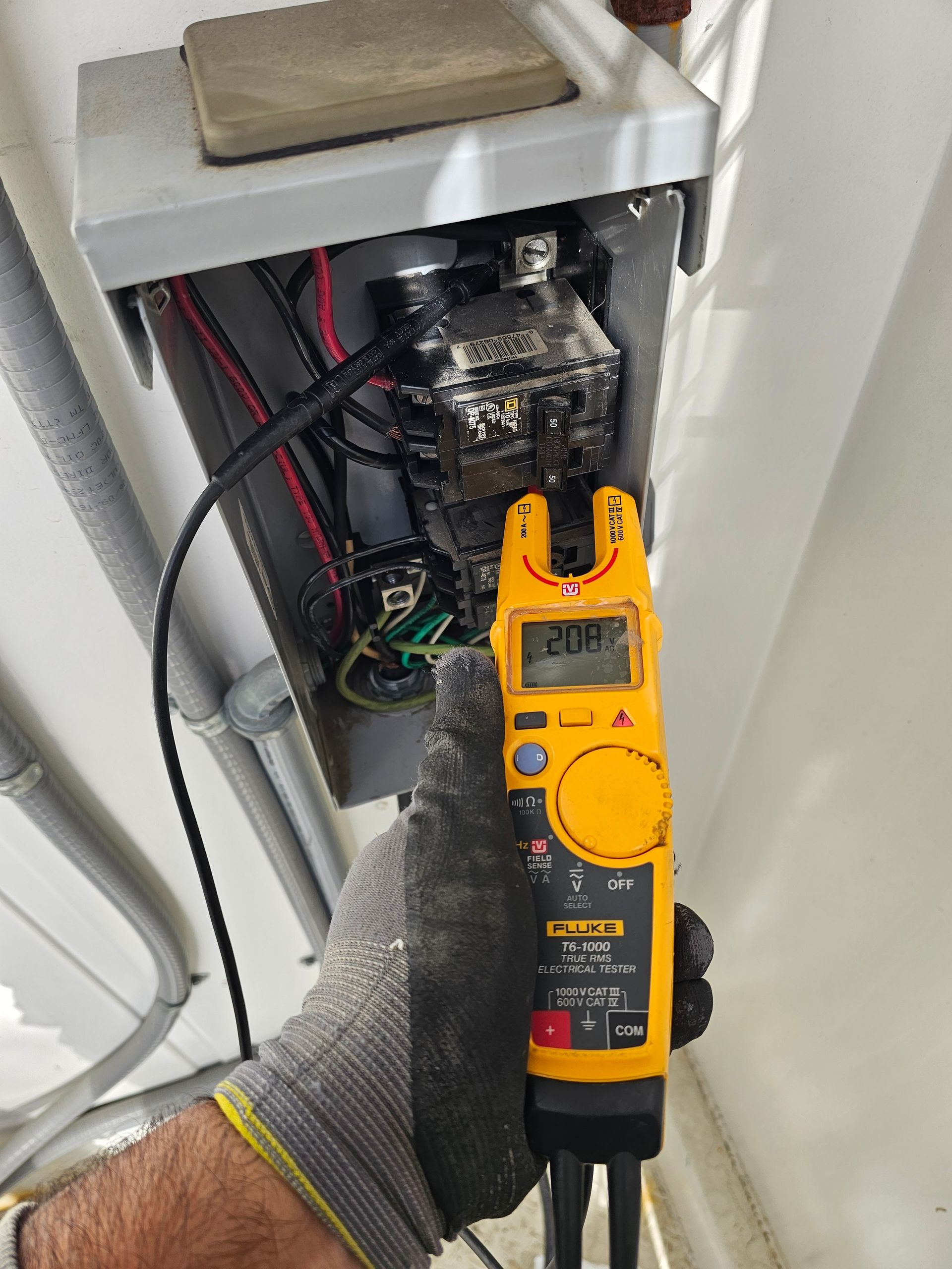 A person wearing a glove tests electrical voltage with a meter in an open electrical box.