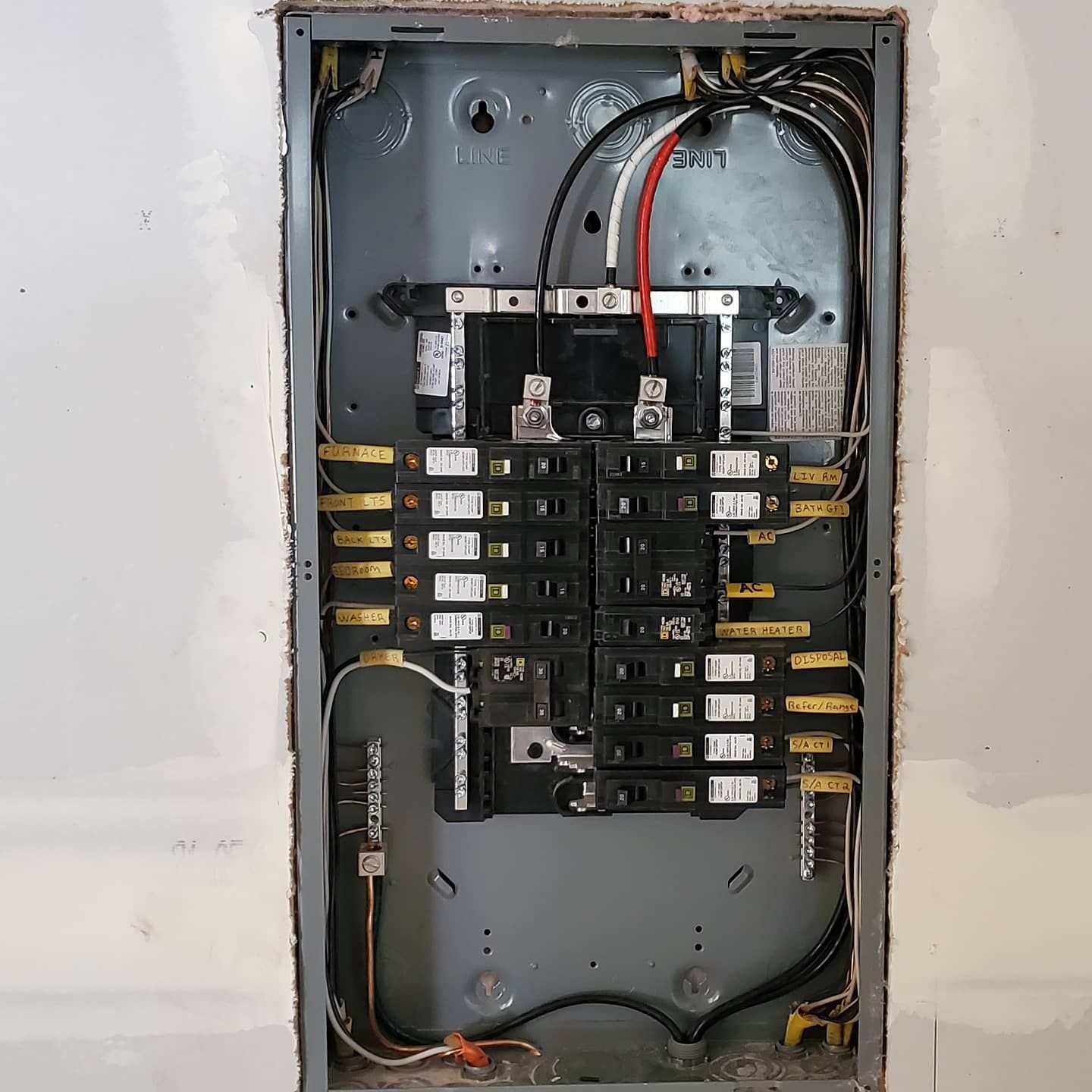 Electrical panel installed in a wall opening, featuring circuit breakers and wiring.