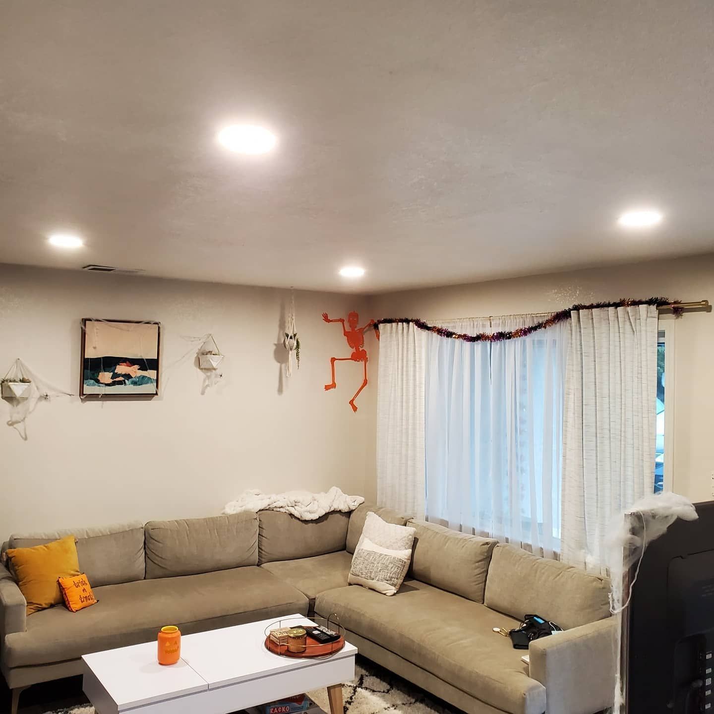 Living room with a tan sectional sofa, white curtains, and Halloween decorations.