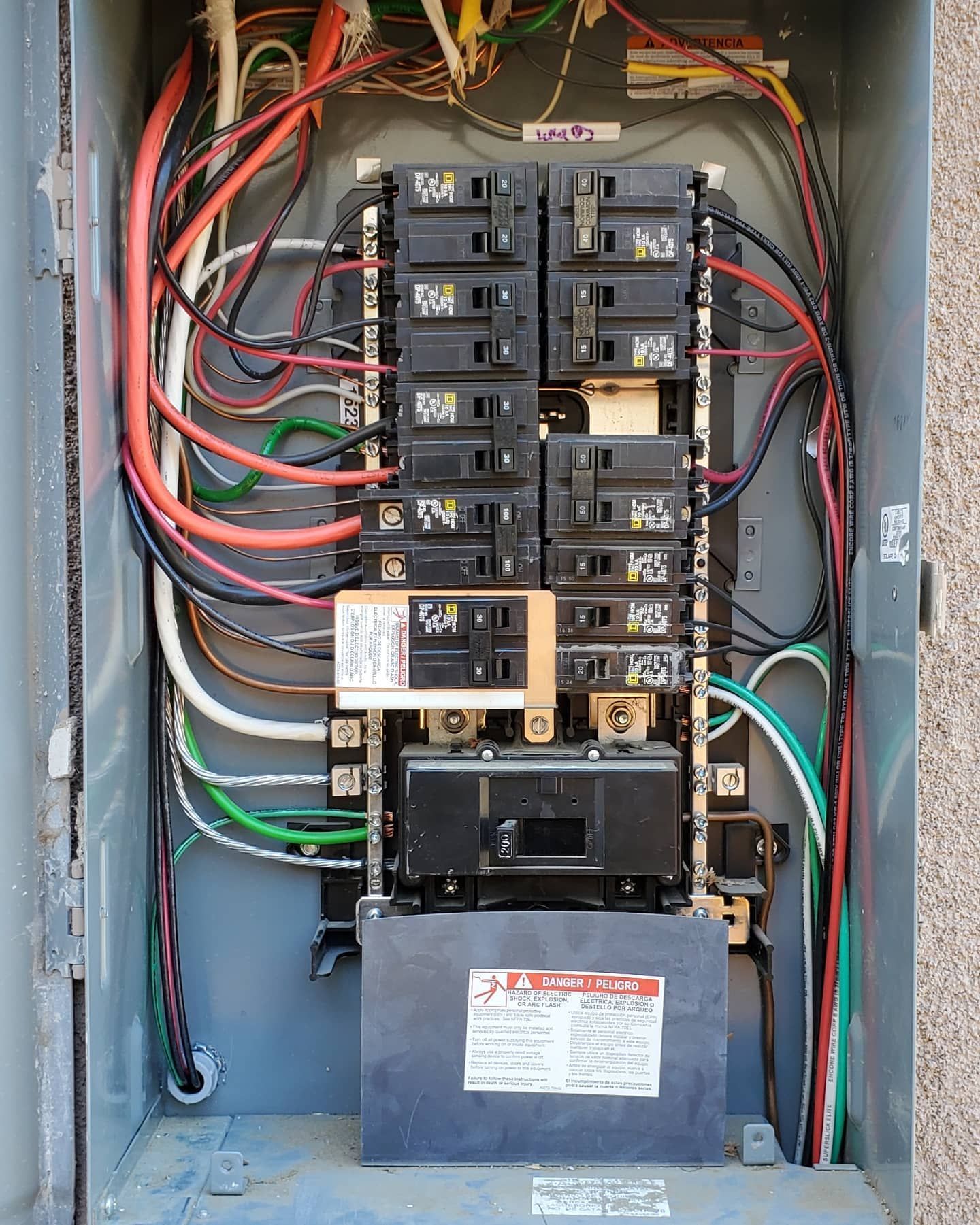 Electrical panel with circuit breakers and wires inside a metal box.