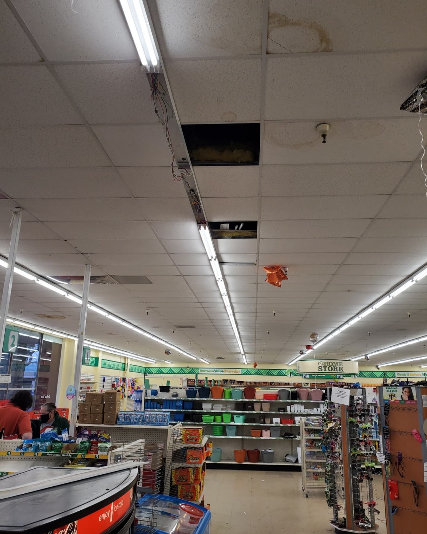A store interior with a damaged ceiling panel. Fluorescent lights illuminate merchandise on shelves.