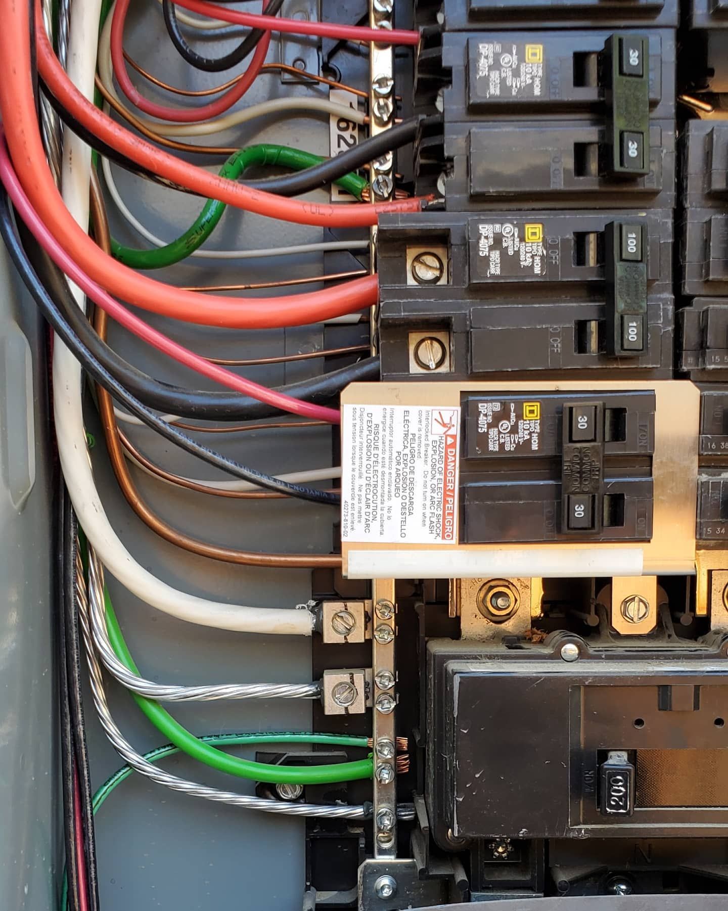 Electrical panel with wires and circuit breakers. Red, black, and white wires visible.