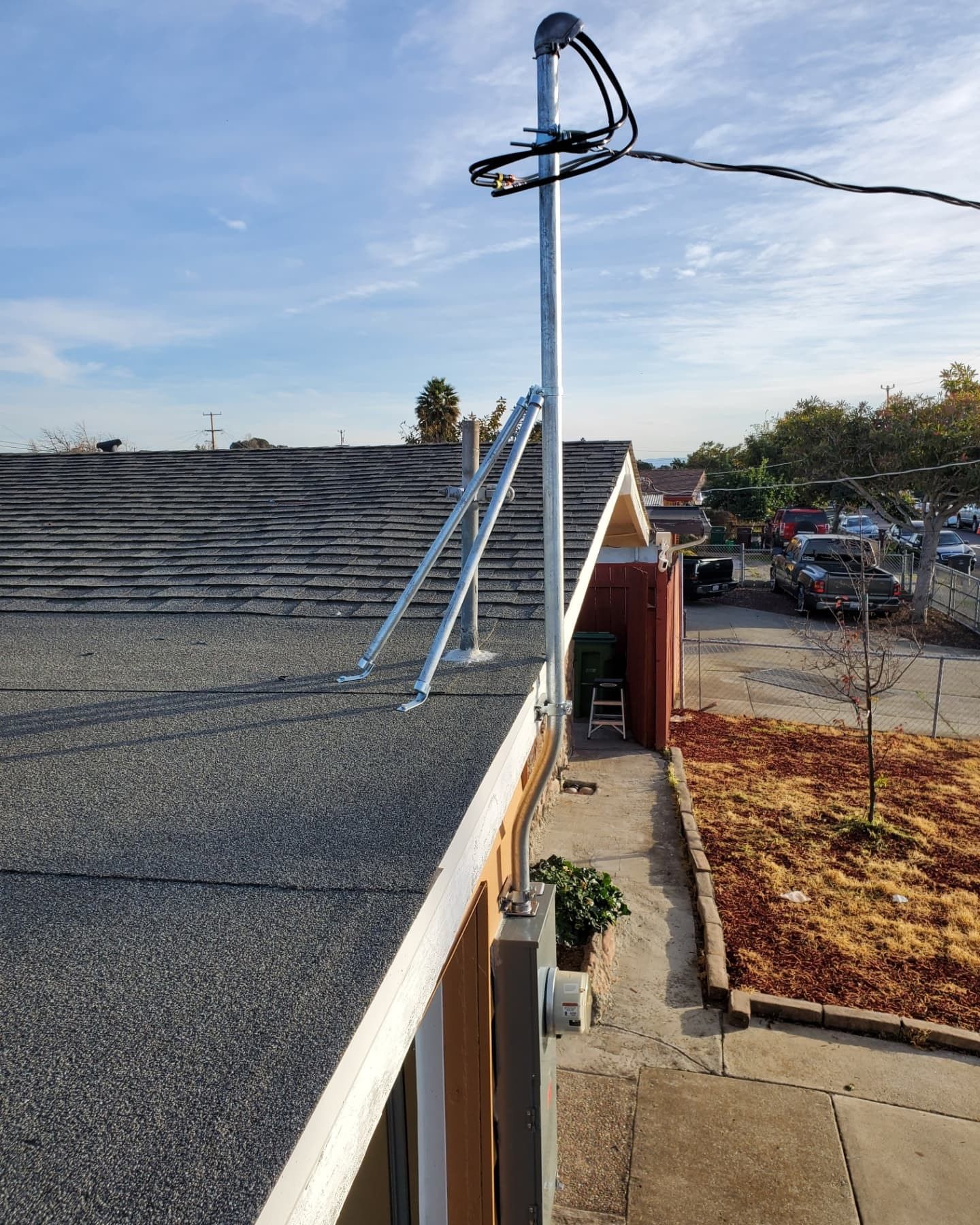 A tall metal pole with cables and roof supports, installed on a dark rooftop. Sunny outdoor setting.