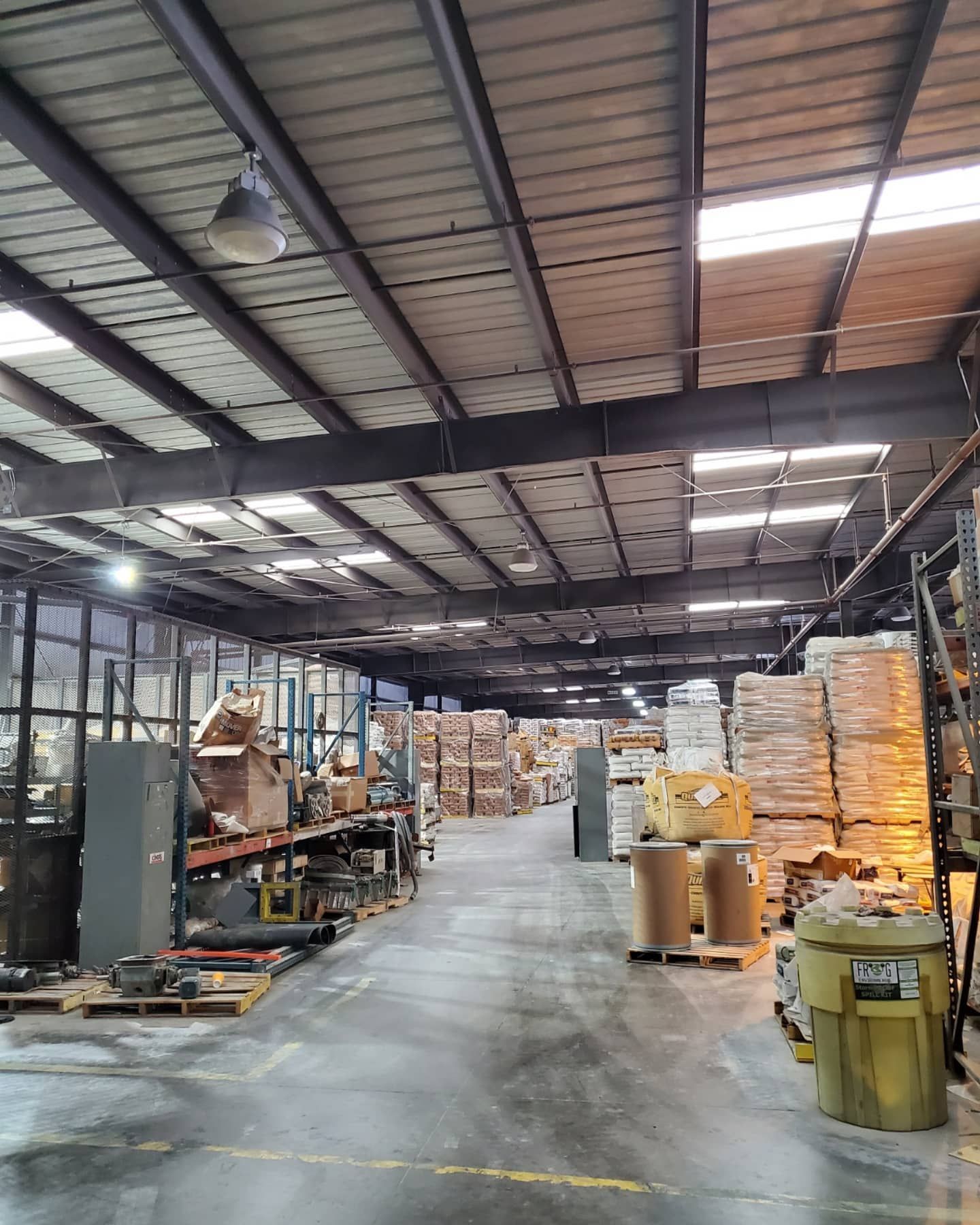 Warehouse interior with metal beams, rows of packed pallets, and various machinery.