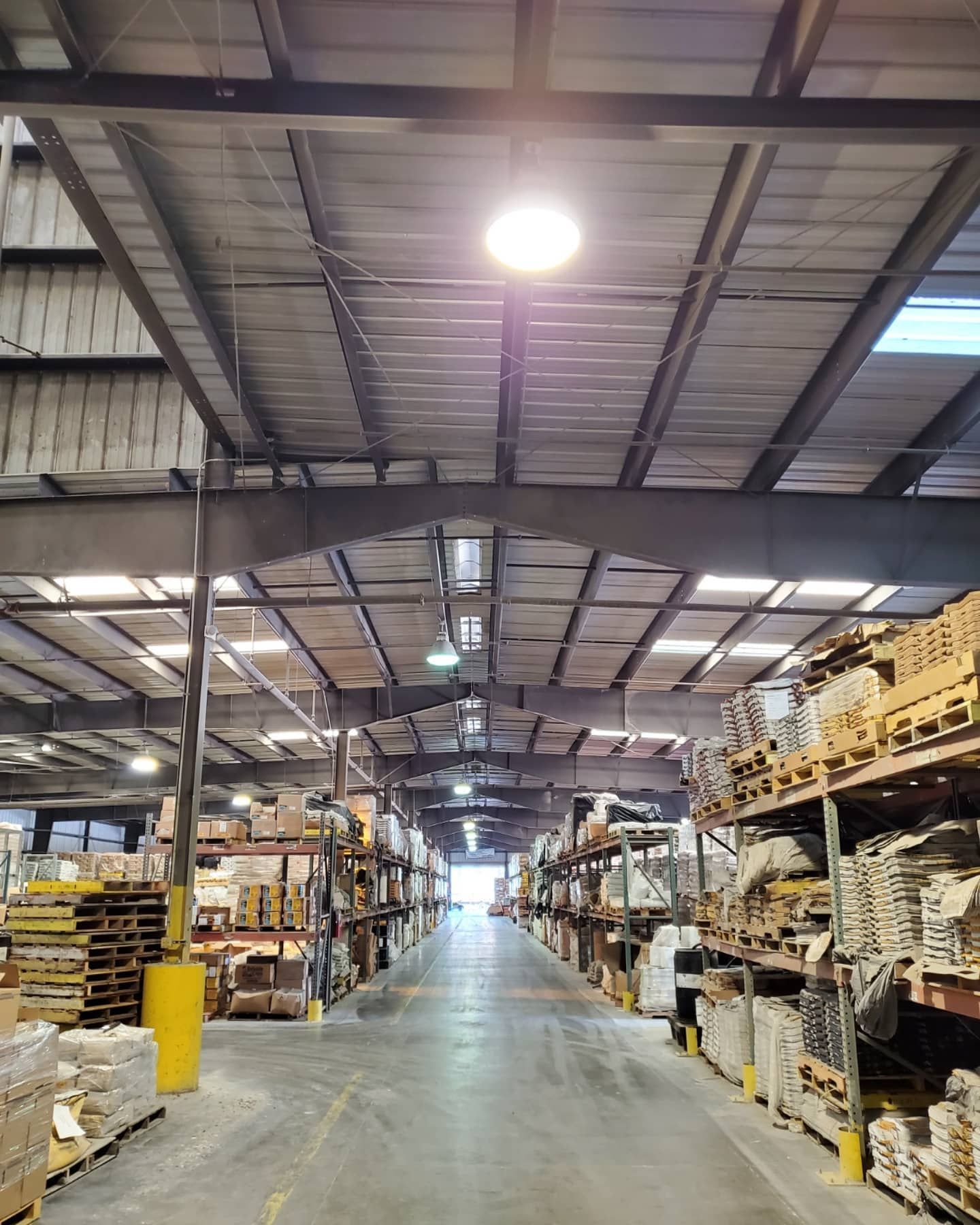 Warehouse interior with rows of shelves holding building materials, metal beams overhead, bright overhead lights.