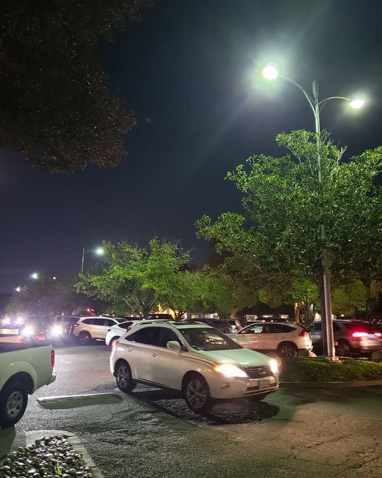 Cars in a parking lot at night, illuminated by streetlights. Trees and a dark sky are in the background.