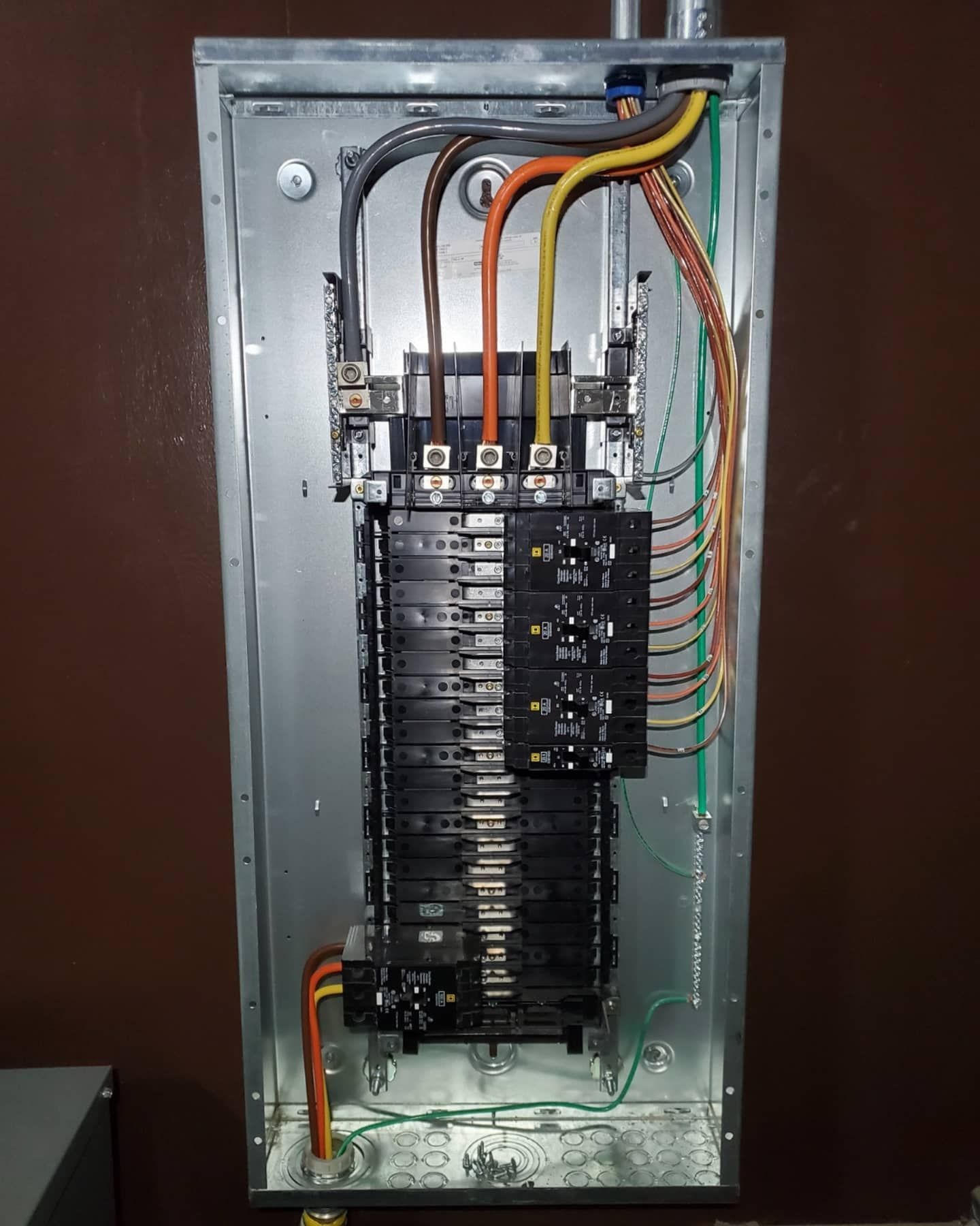 Electrical panel with wires and circuit breakers. Gray metal box mounted on a brown wall.
