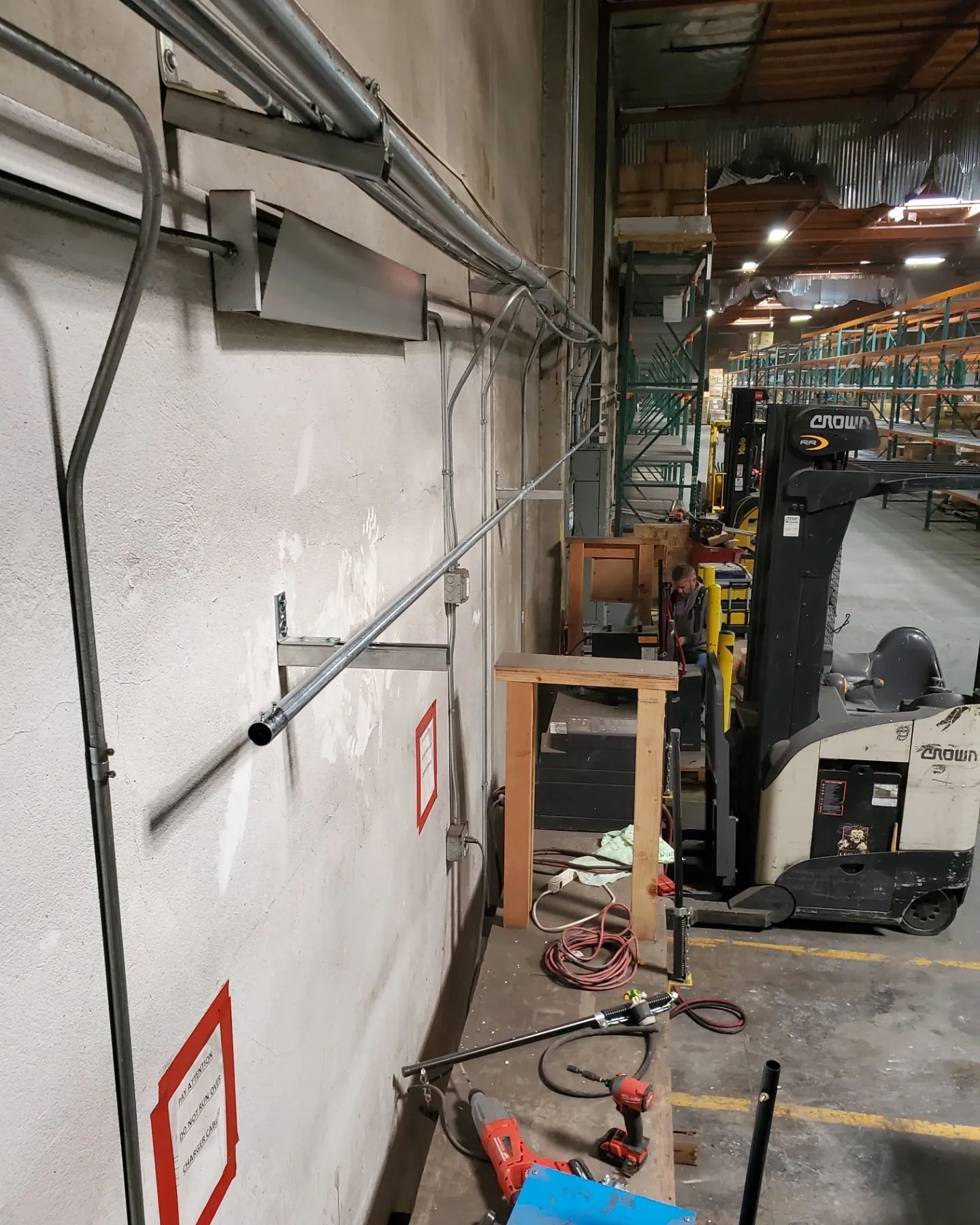Electrical conduit installation on a warehouse wall. A forklift and tools are visible in the background.
