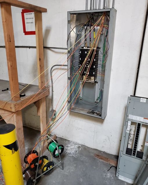 Electrical panel with loose wires, spools of colored wire, and a wooden structure.