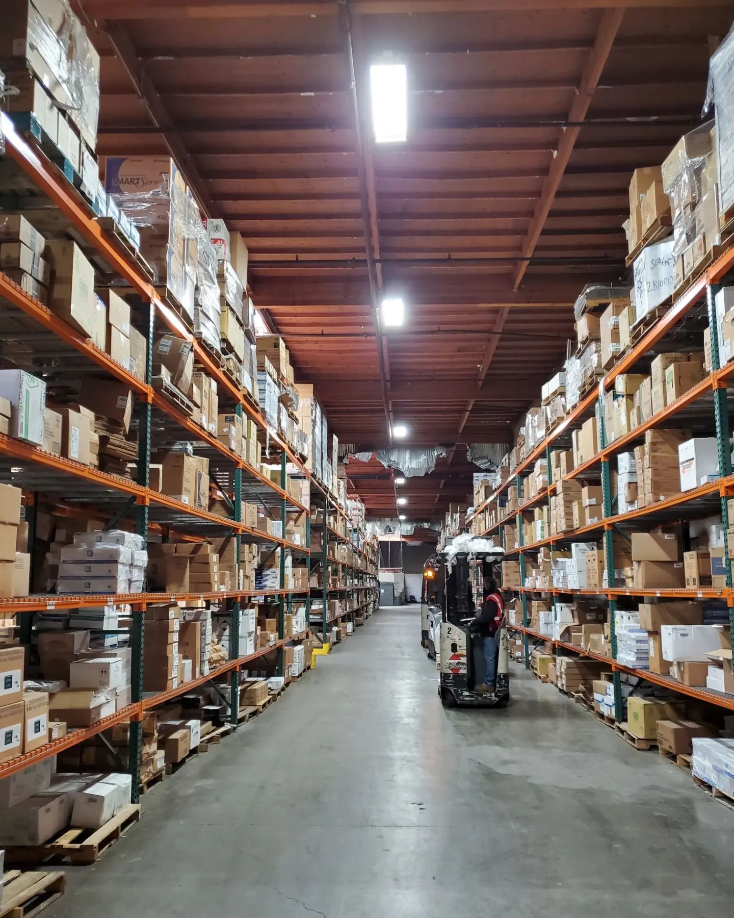 Warehouse interior with rows of shelves filled with boxes; person on motorized cart in the aisle.