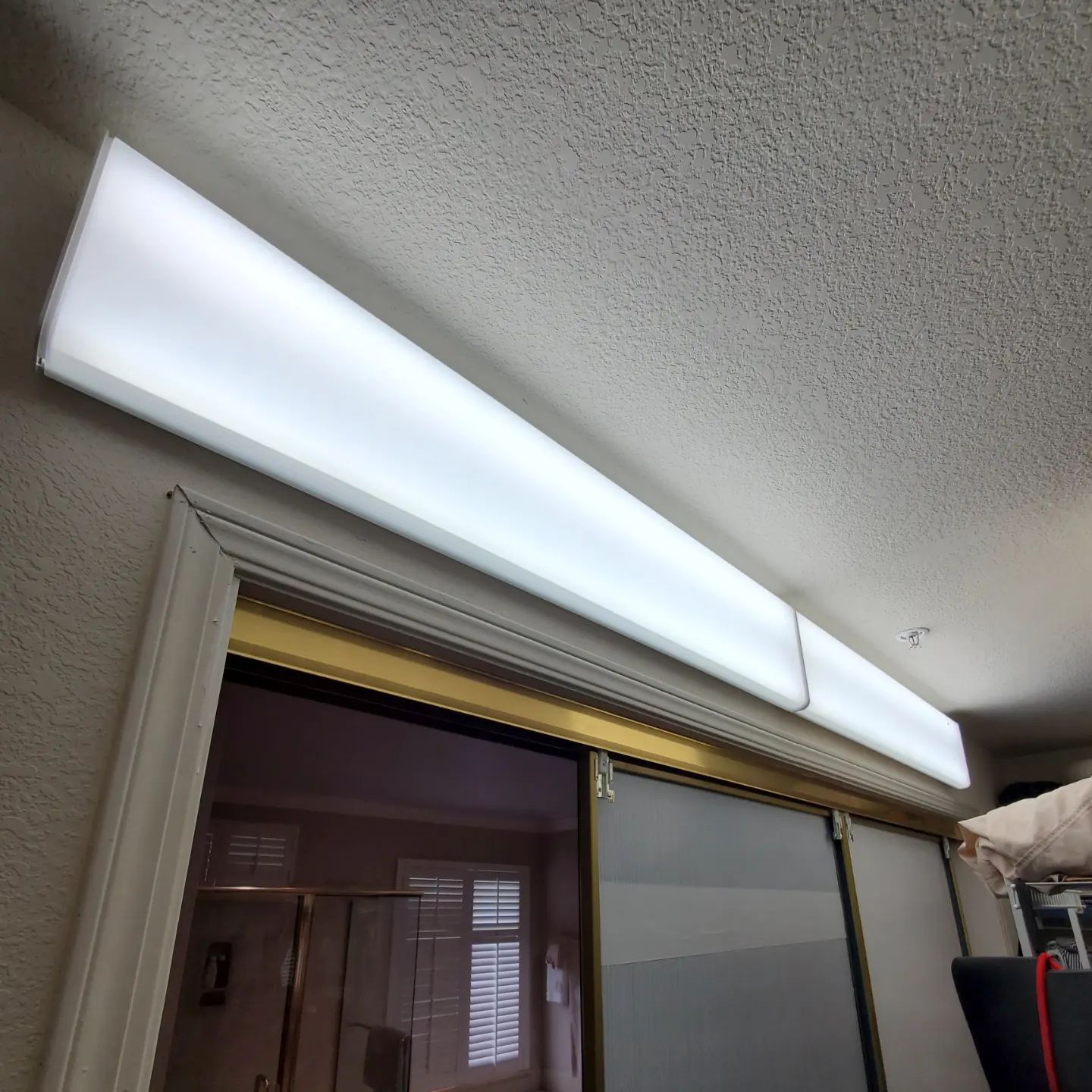 Long, white fluorescent light fixture mounted above sliding glass door.