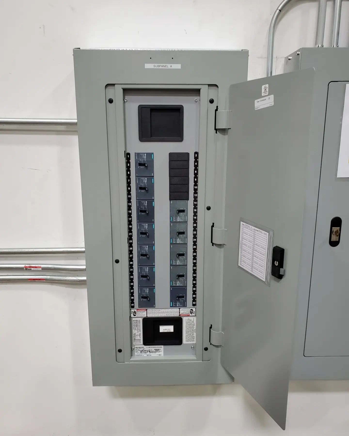 Electrical breaker panel with the door open, mounted on a white wall.
