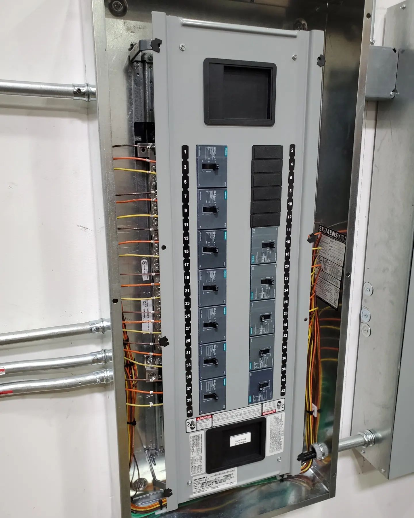Electrical panel with circuit breakers and wiring. Installed in a wall, with metal conduit nearby.