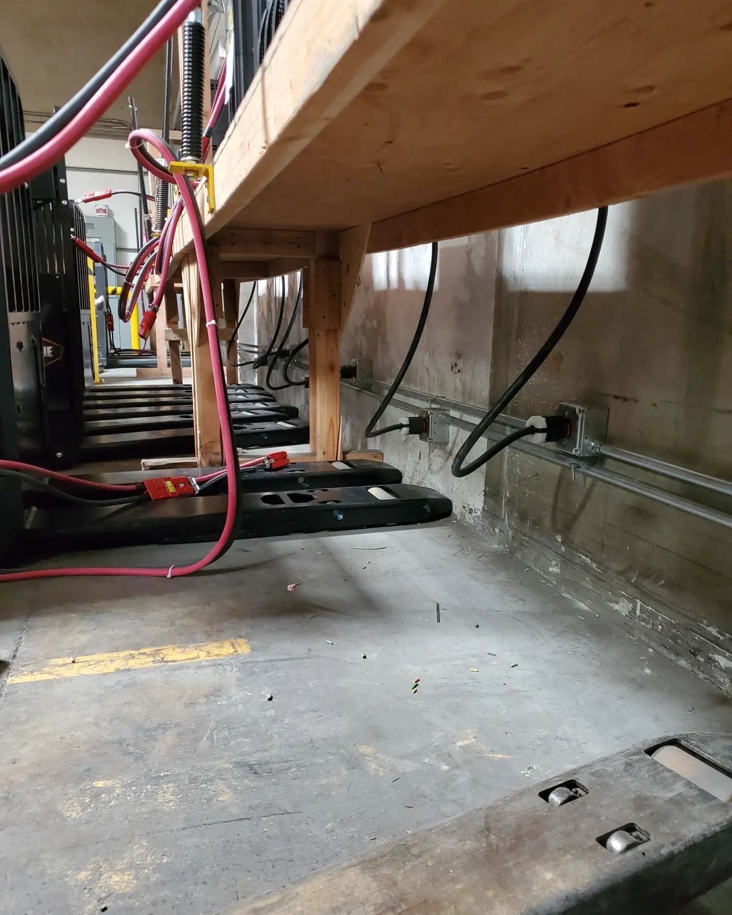 Batteries on wooden shelving, wires, and conduits in a cement-walled room.