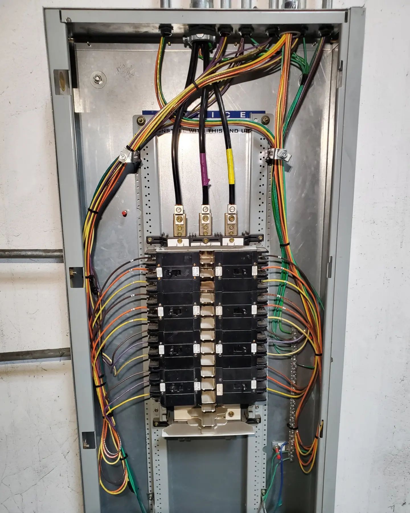 Electrical panel with wires of various colors, mounted on a wall.