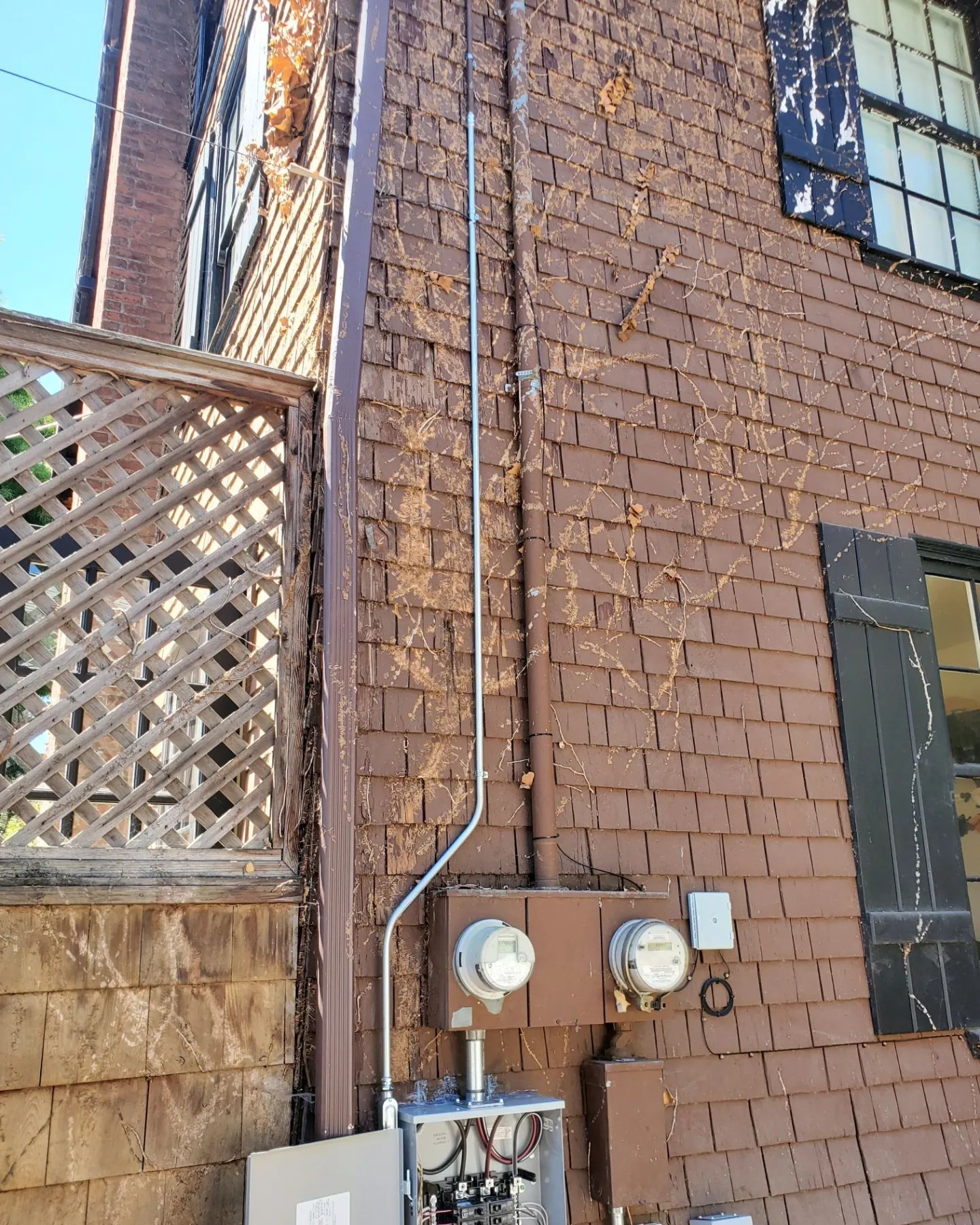 Exterior view of a brown brick building with electrical meters and conduit, trellis, and windows.
